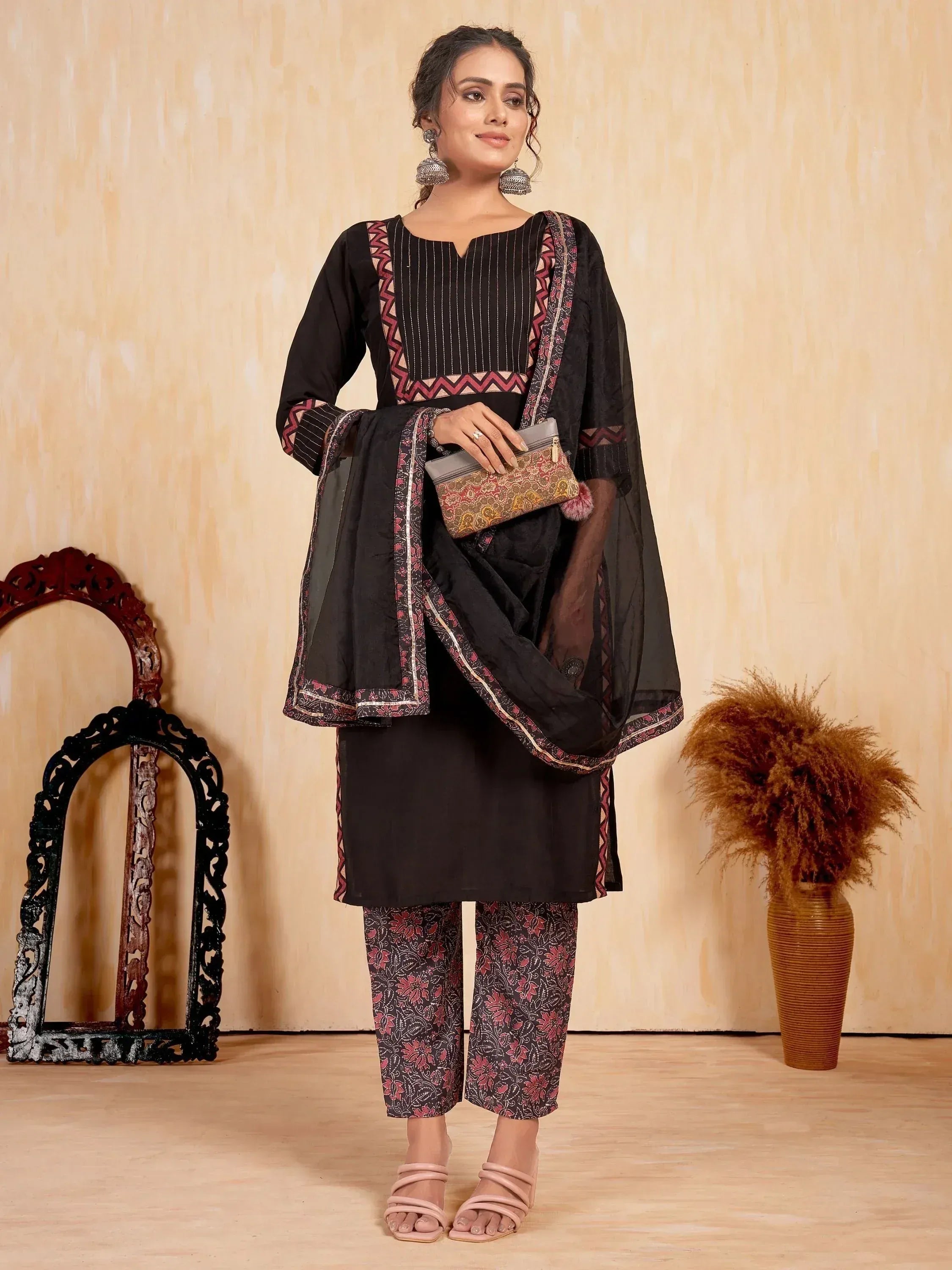 Black ethnic salwar kameez with floral pants and embroidered dupatta, styled with jhumka earrings and clutch