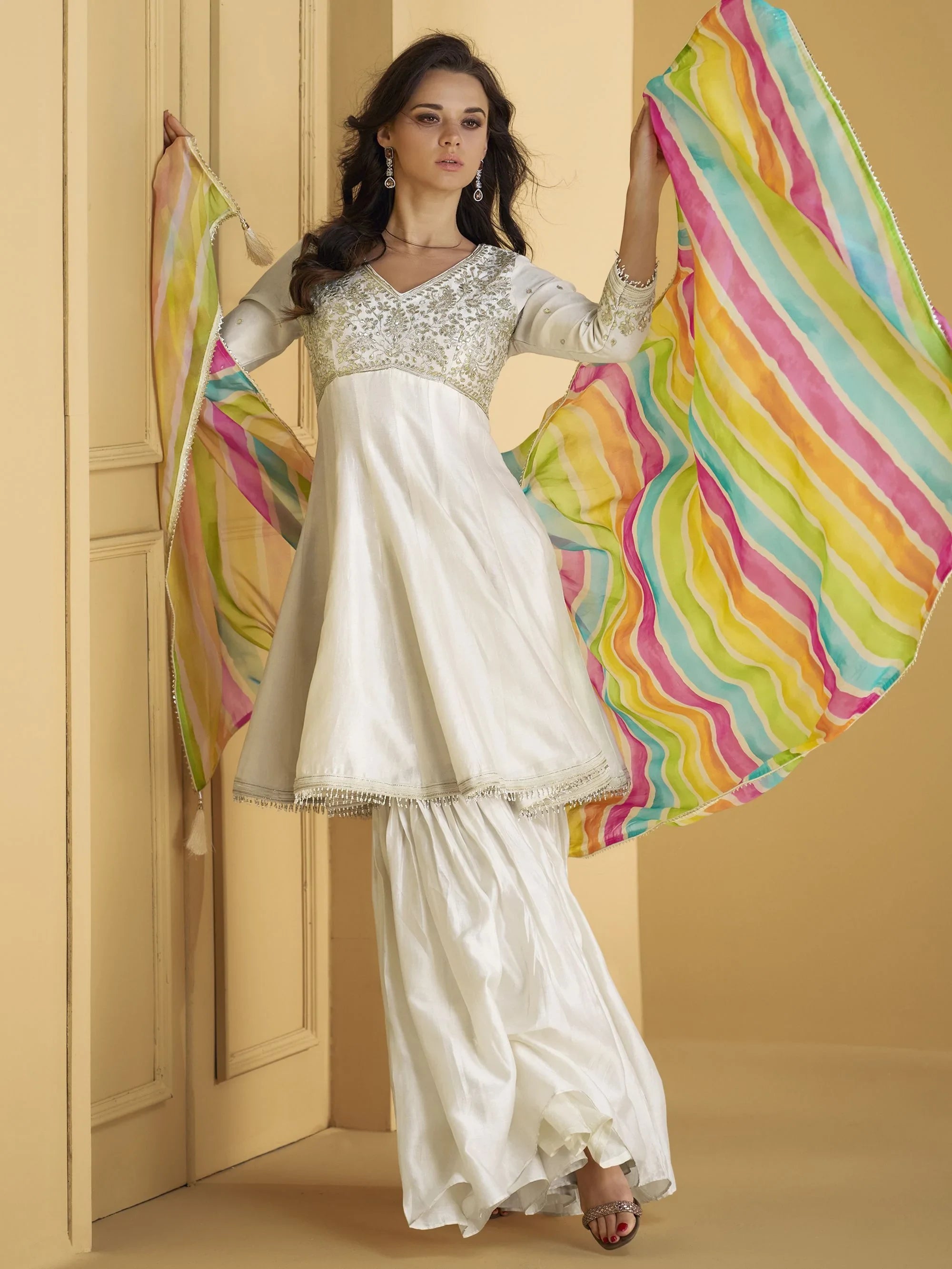 Woman in white sharara suit with sequins and colorful dupatta, ethnic Indian wear.