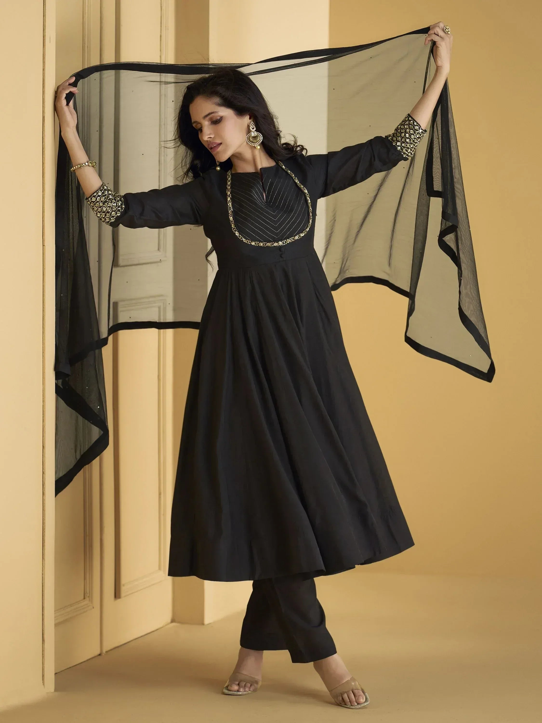 Black ethnic gown with gold embroidery and sheer dupatta, styled with palazzo pants for festive occasions.