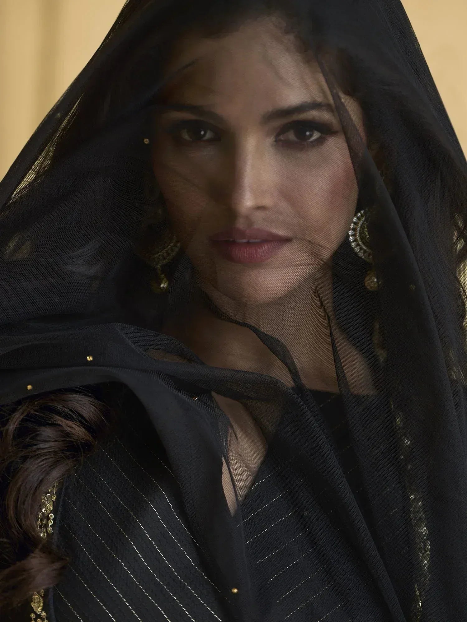 Elegant black ethnic gown with sheer dupatta and gold embroidery, styled with traditional earrings.