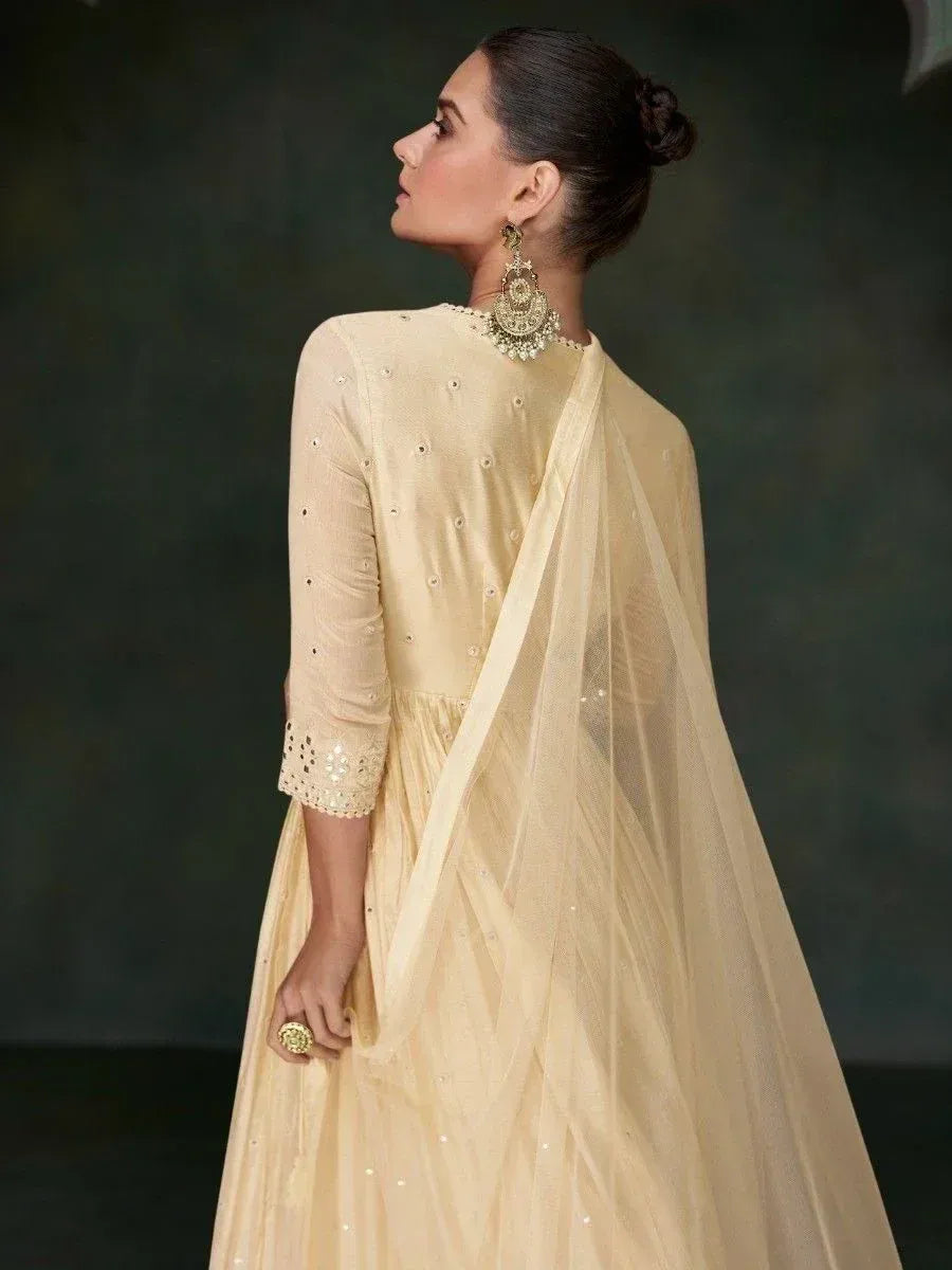 Elegant cream ethnic gown with mirror work and sheer dupatta, styled with jhumka earrings for Indian occasions