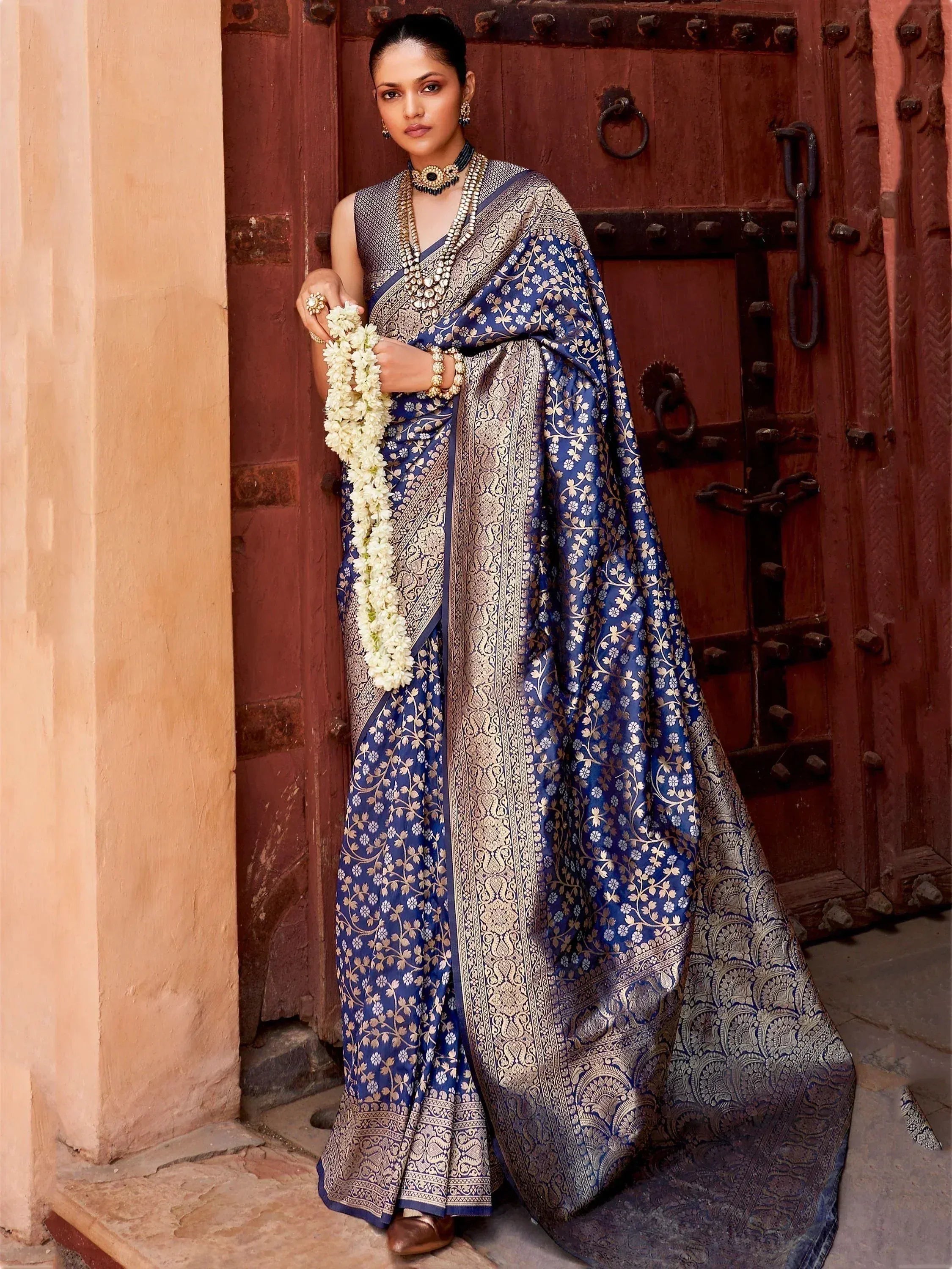 Blue and gold floral Banarasi saree with heavy zari work, styled with traditional jewelry and jasmine garland.