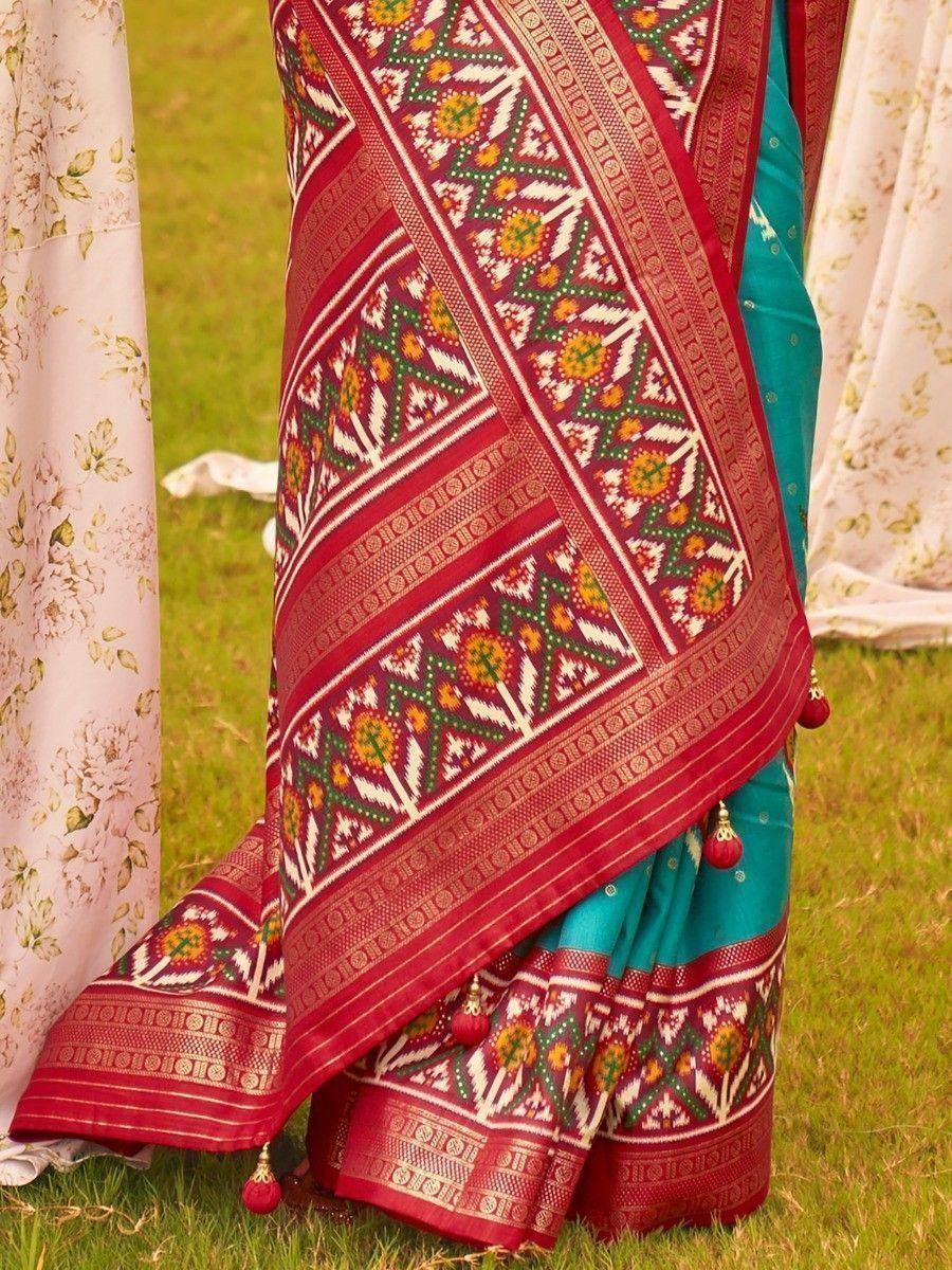 Teal saree with red geometric border, floral motifs, and tassels, perfect for ethnic occasions