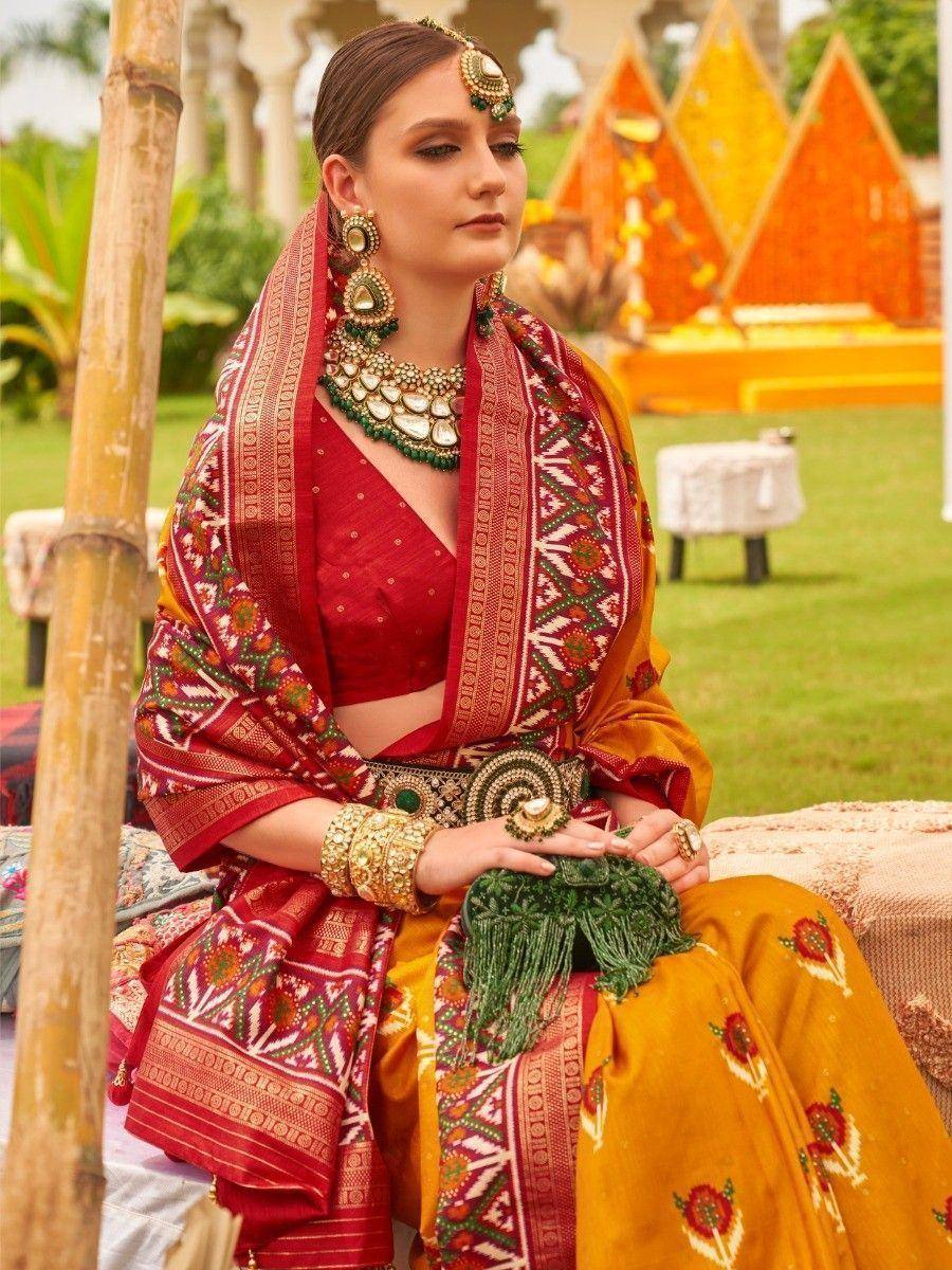 Woman in red and gold embroidered lehenga choli with green jewelry, traditional Indian ethnic wear
