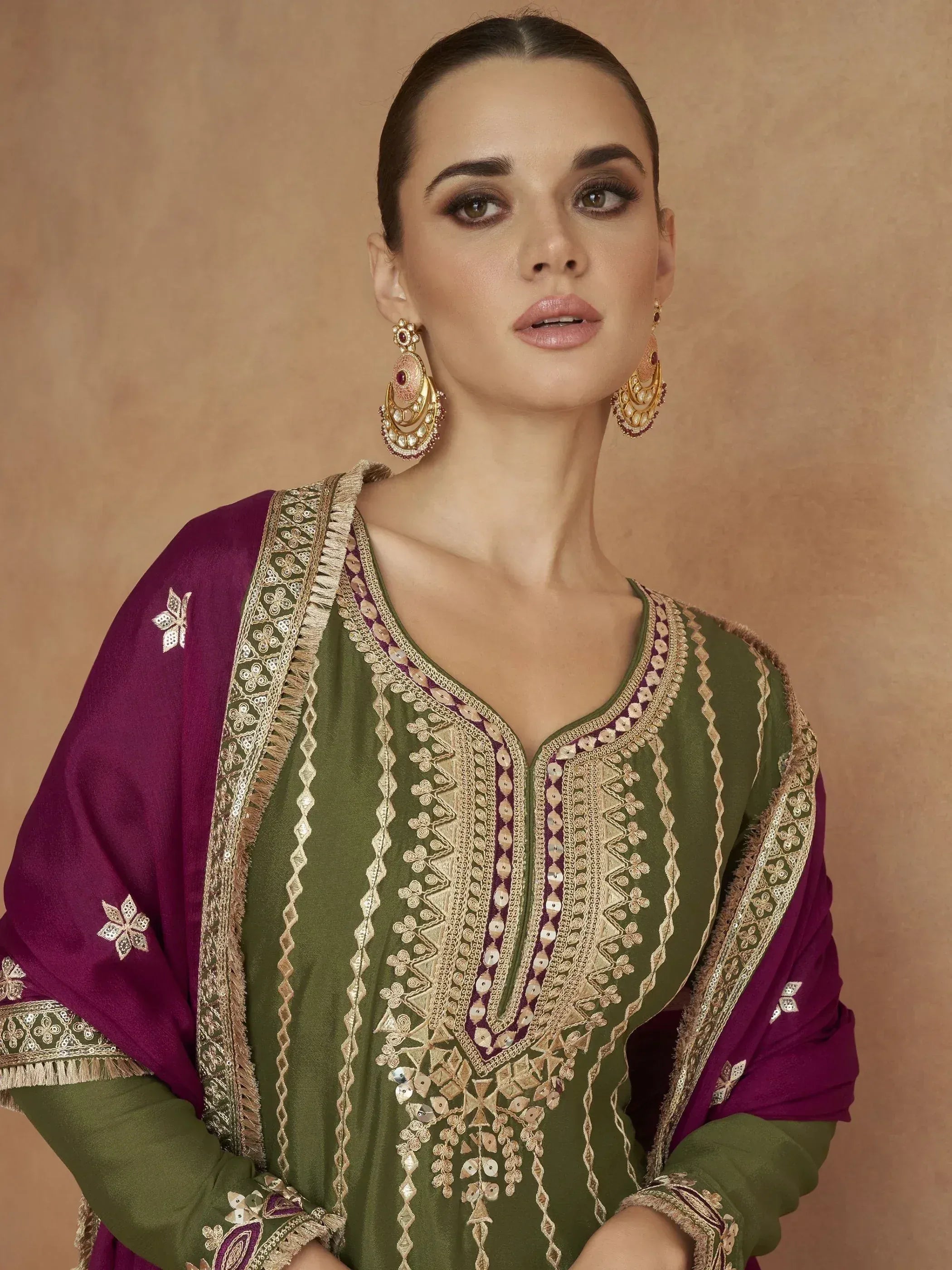Green and maroon embroidered salwar kameez with gold detailing and matching dupatta, styled with traditional jhumka earrings.
