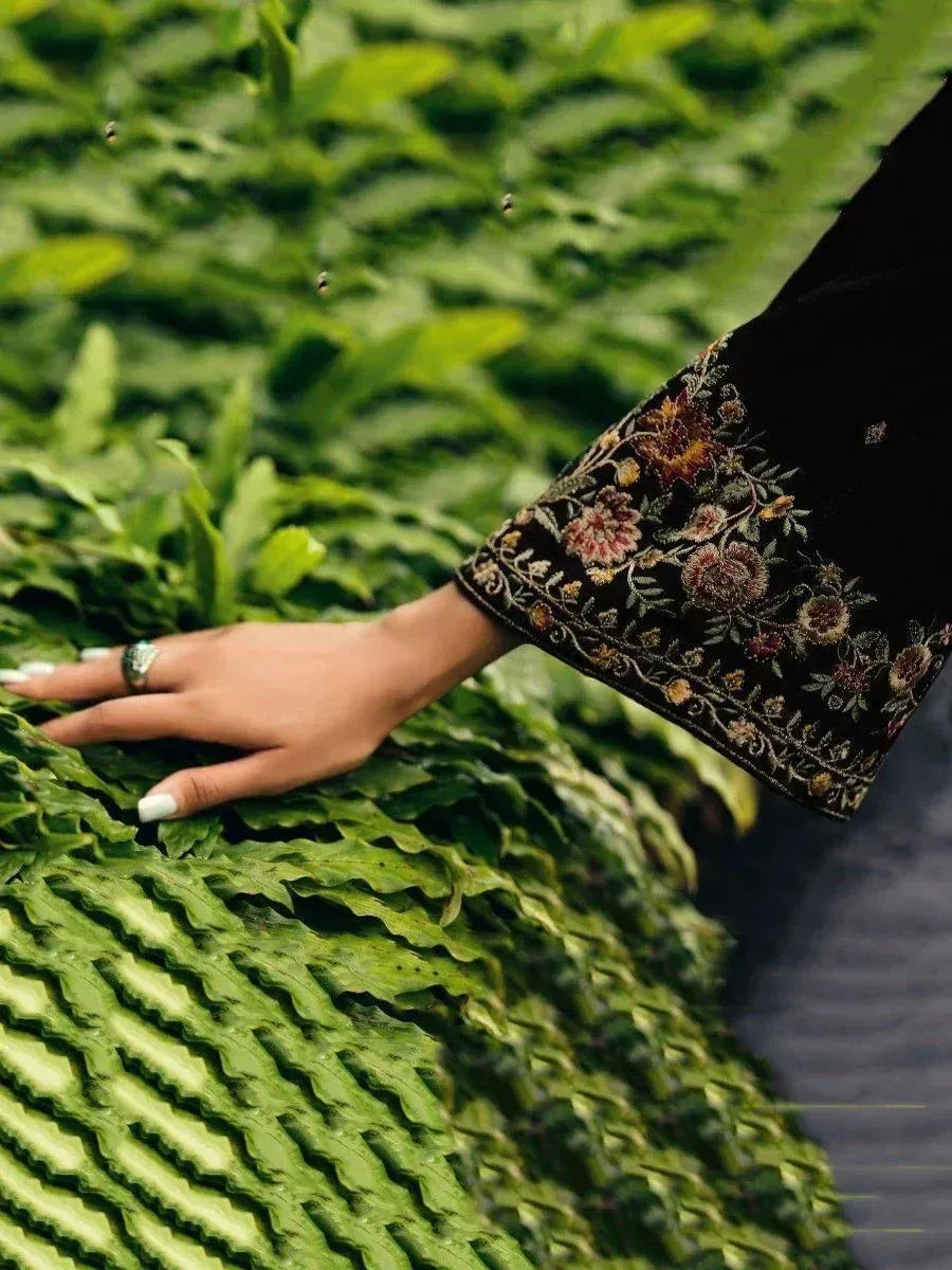 Elegant black sleeve with floral embroidery, hand resting on green foliage