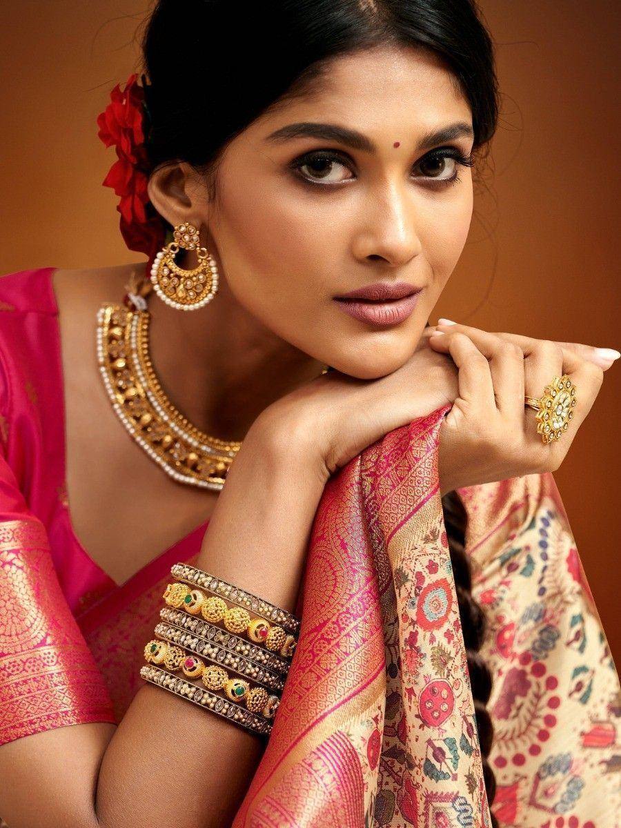 Woman in vibrant pink ethnic saree with gold jewelry, floral hair accessory, and traditional bangles