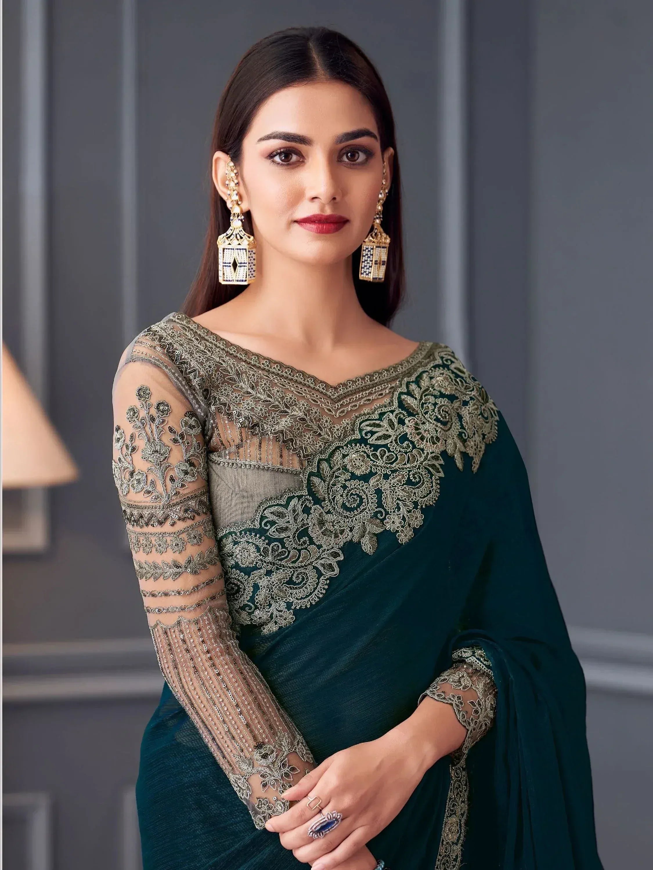 Elegant emerald green saree with intricate gold embroidery and sheer sleeves, paired with statement earrings.
