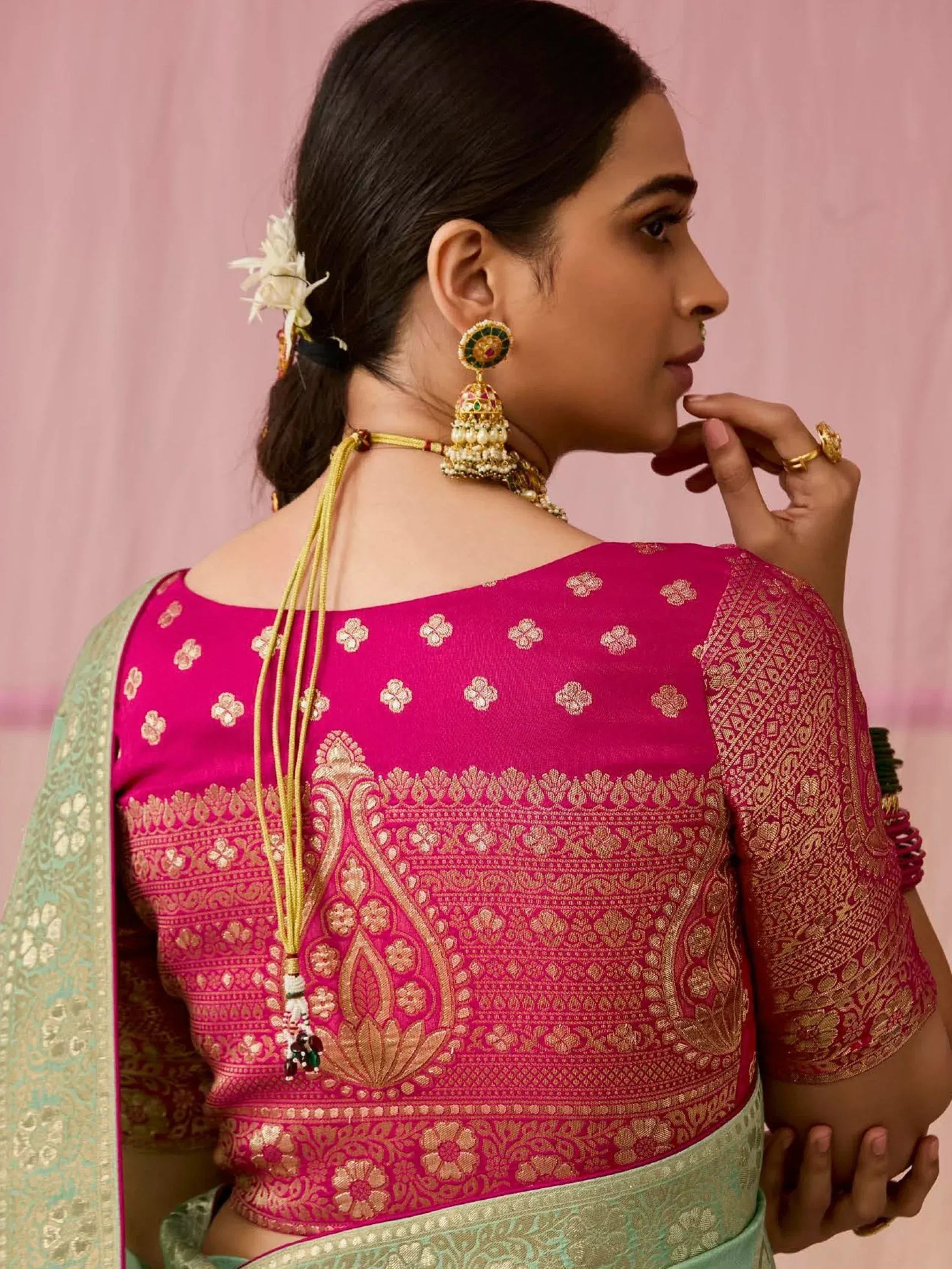Pink and gold embroidered saree blouse with traditional Indian jewelry and floral hair accessory