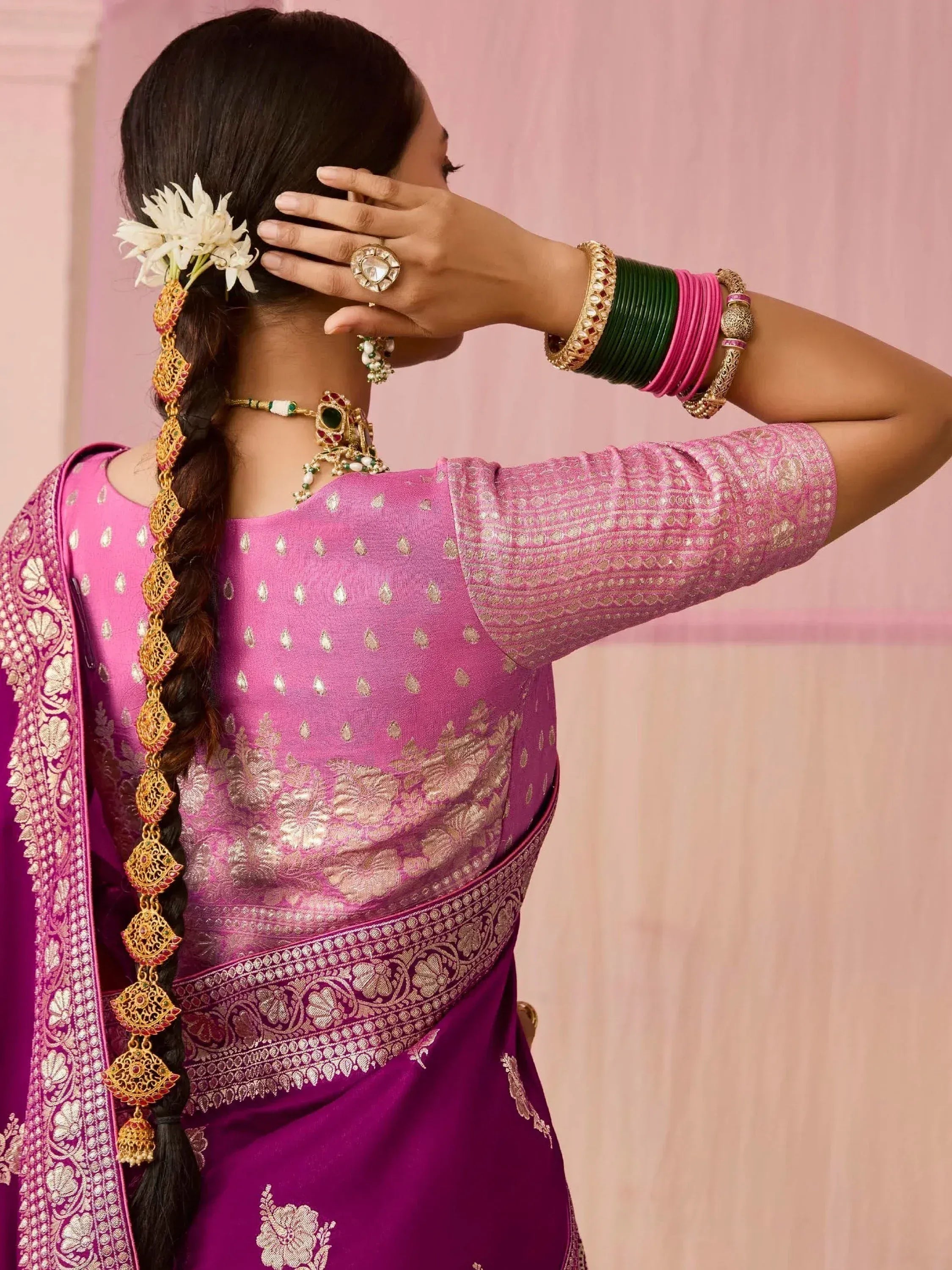 Woman in pink ethnic saree with gold embroidery, floral hair accessory, and traditional jewelry