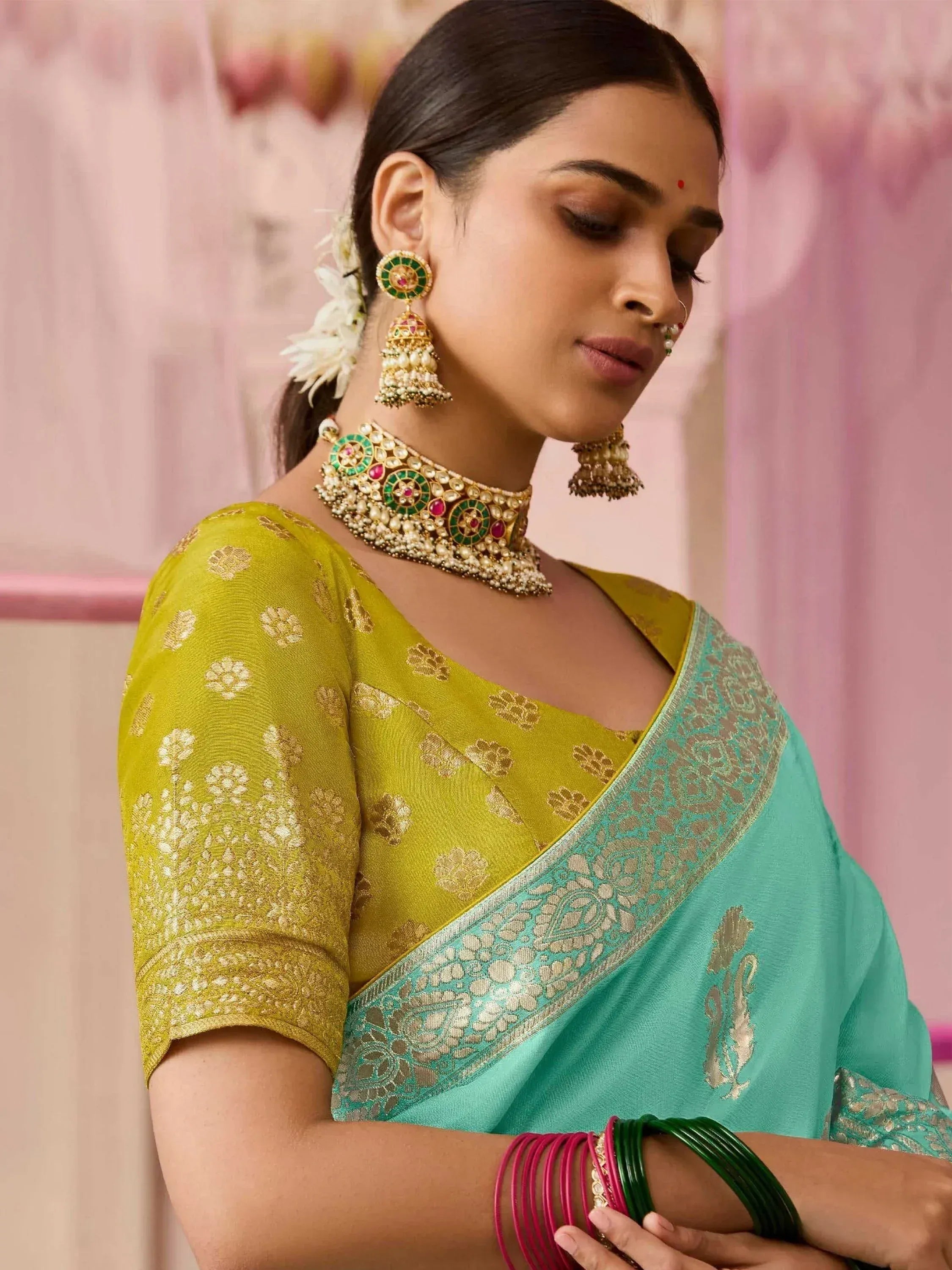 Woman in green and yellow designer saree with gold embroidery, traditional jewelry, and floral hair accessory