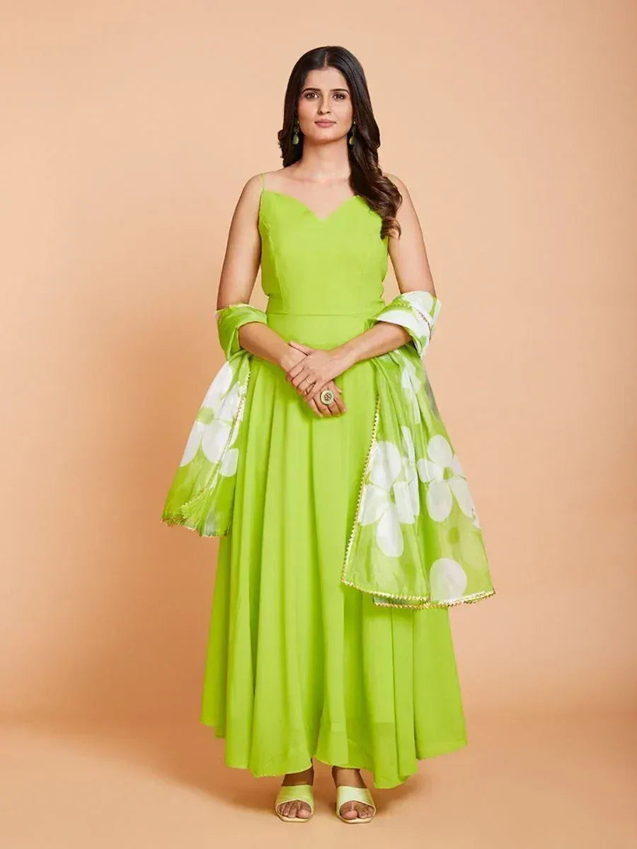 Woman in lime green ethnic gown with dupatta and floral pattern, standing against peach background