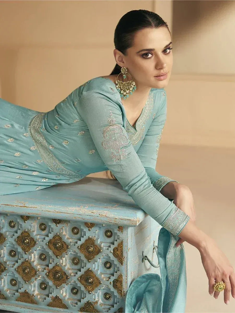 Woman in light blue embroidered salwar kameez with gold detailing, styled with statement earrings and ring
