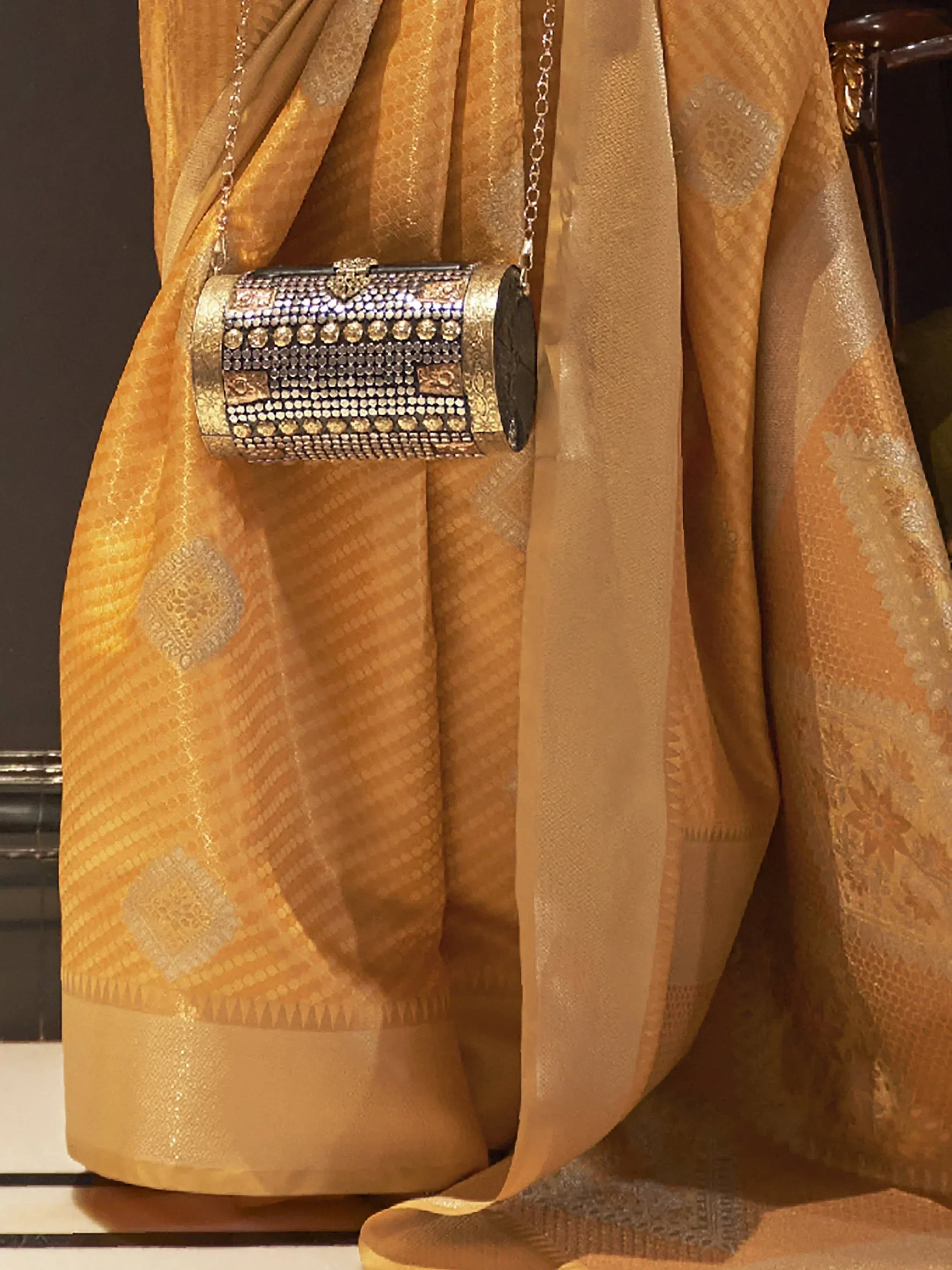 Elegant gold saree with intricate patterns paired with a sparkling embellished clutch bag for ethnic wear.
