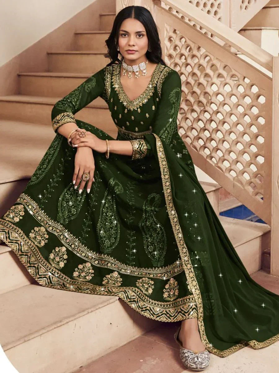 Woman wearing dark green embroidered Indian ethnic gown with gold accents, seated on stairs