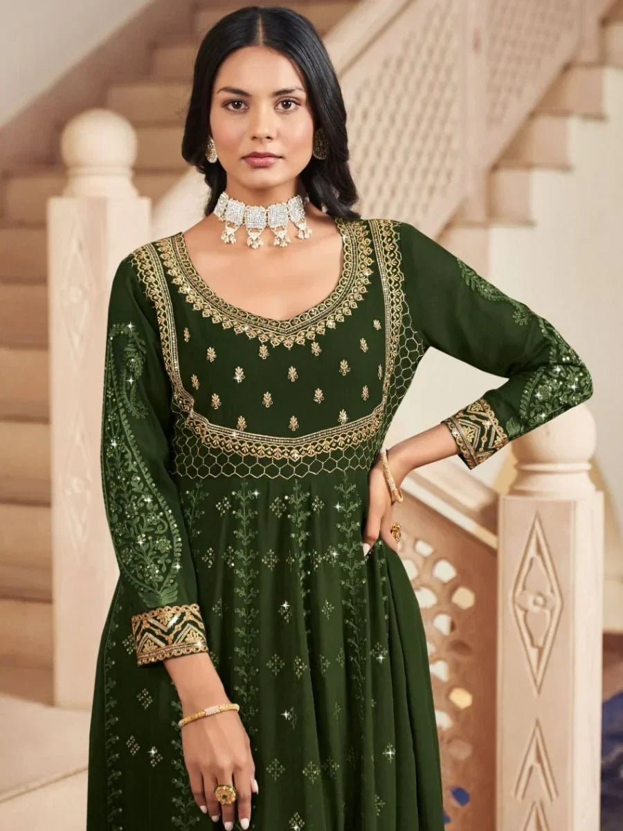 Woman in dark green embroidered Anarkali suit with gold detailing, wearing traditional jewelry.