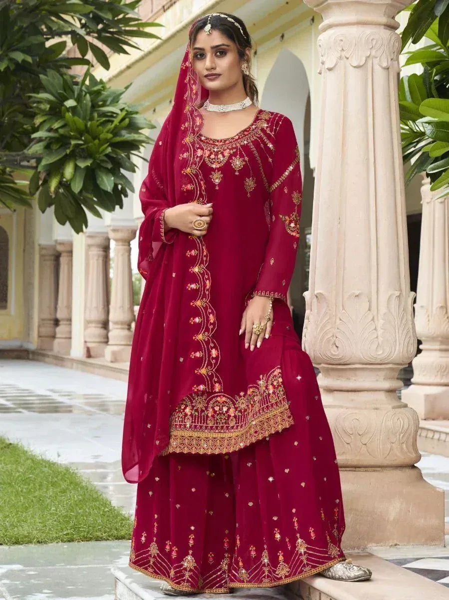Woman in maroon embroidered salwar kameez with gold detailing, traditional jewelry, outdoor setting