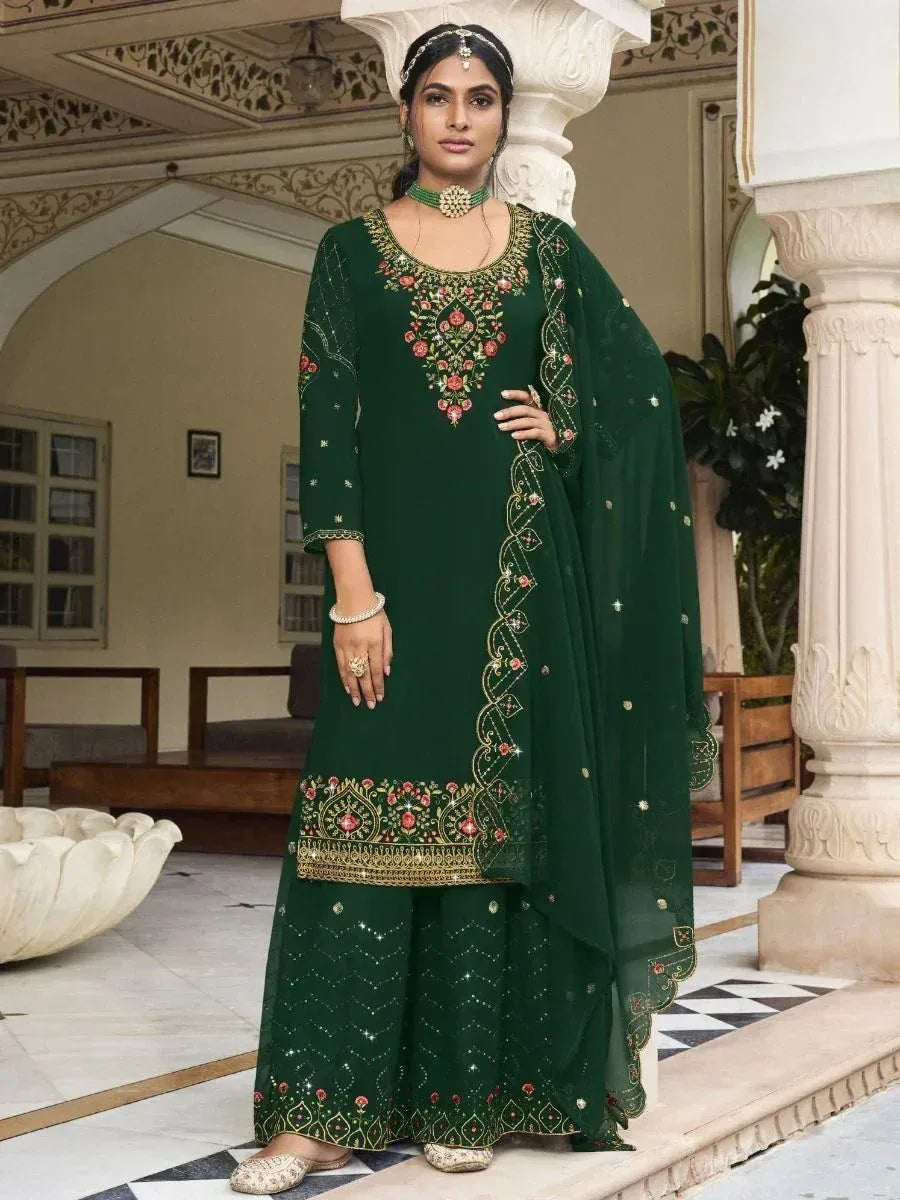 Woman in dark green embroidered salwar kameez with dupatta, standing in courtyard