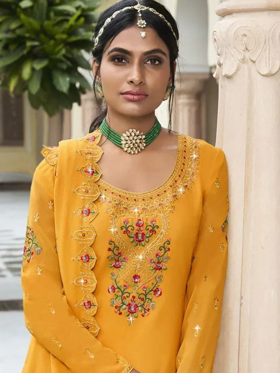Woman in mustard yellow embroidered salwar kameez with floral jewelry and dupatta