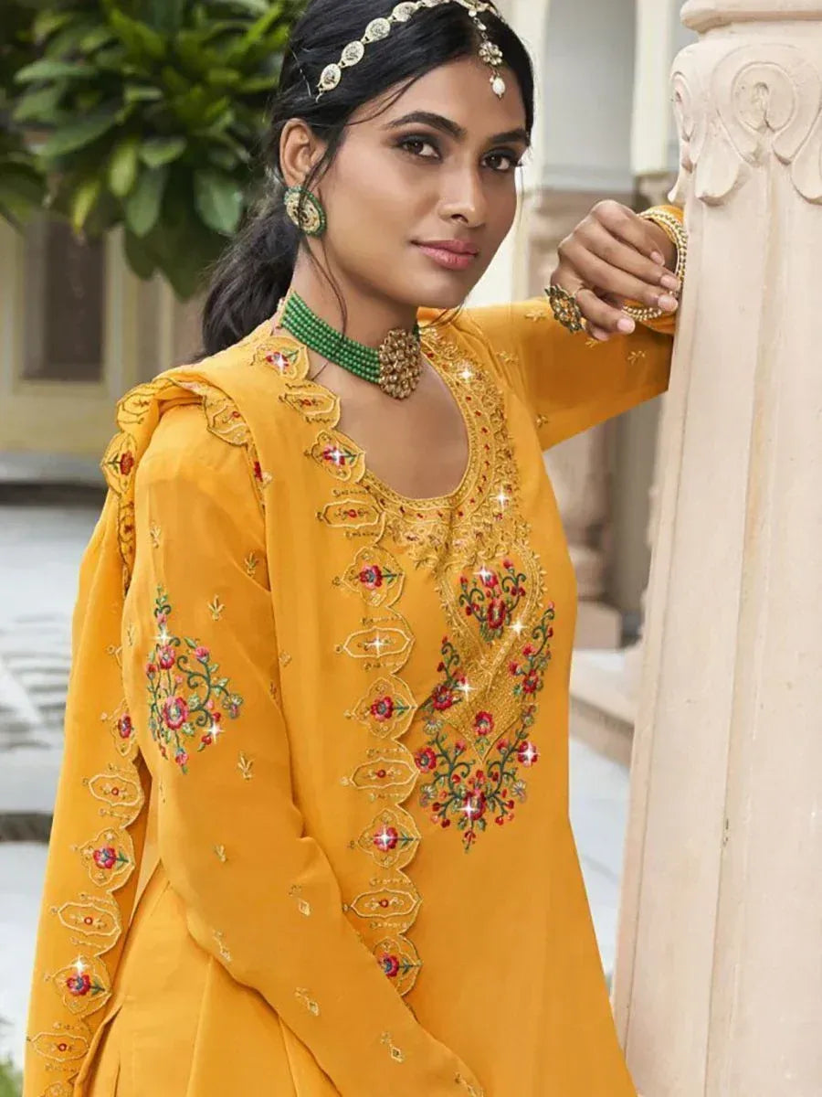 Woman in mustard yellow embroidered salwar kameez with green jewelry, ethnic fashion