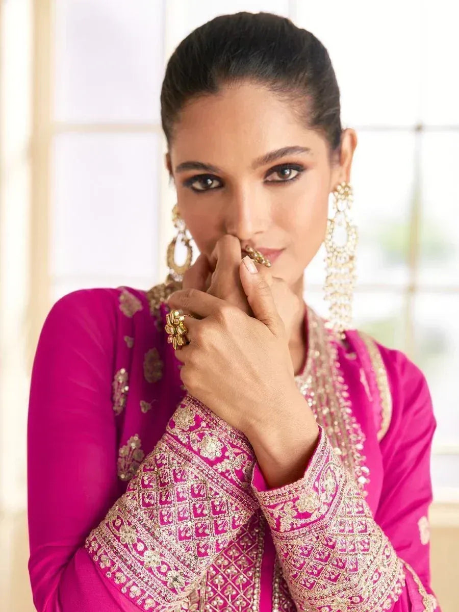 Woman in vibrant pink embroidered ethnic wear with gold jewelry, perfect for festive occasions