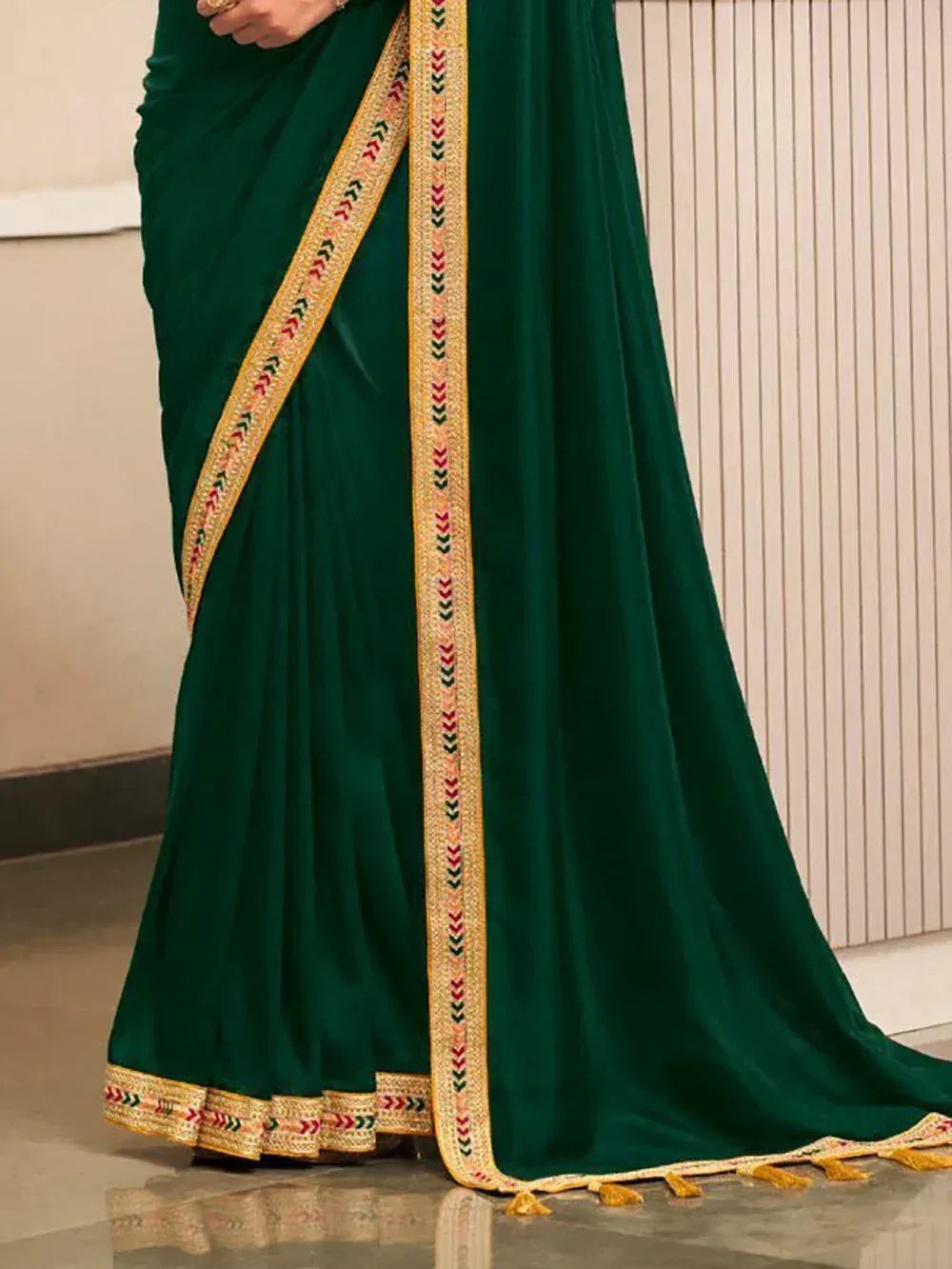 Emerald green velvet saree with gold embroidered border and tassels, ideal for ethnic occasions