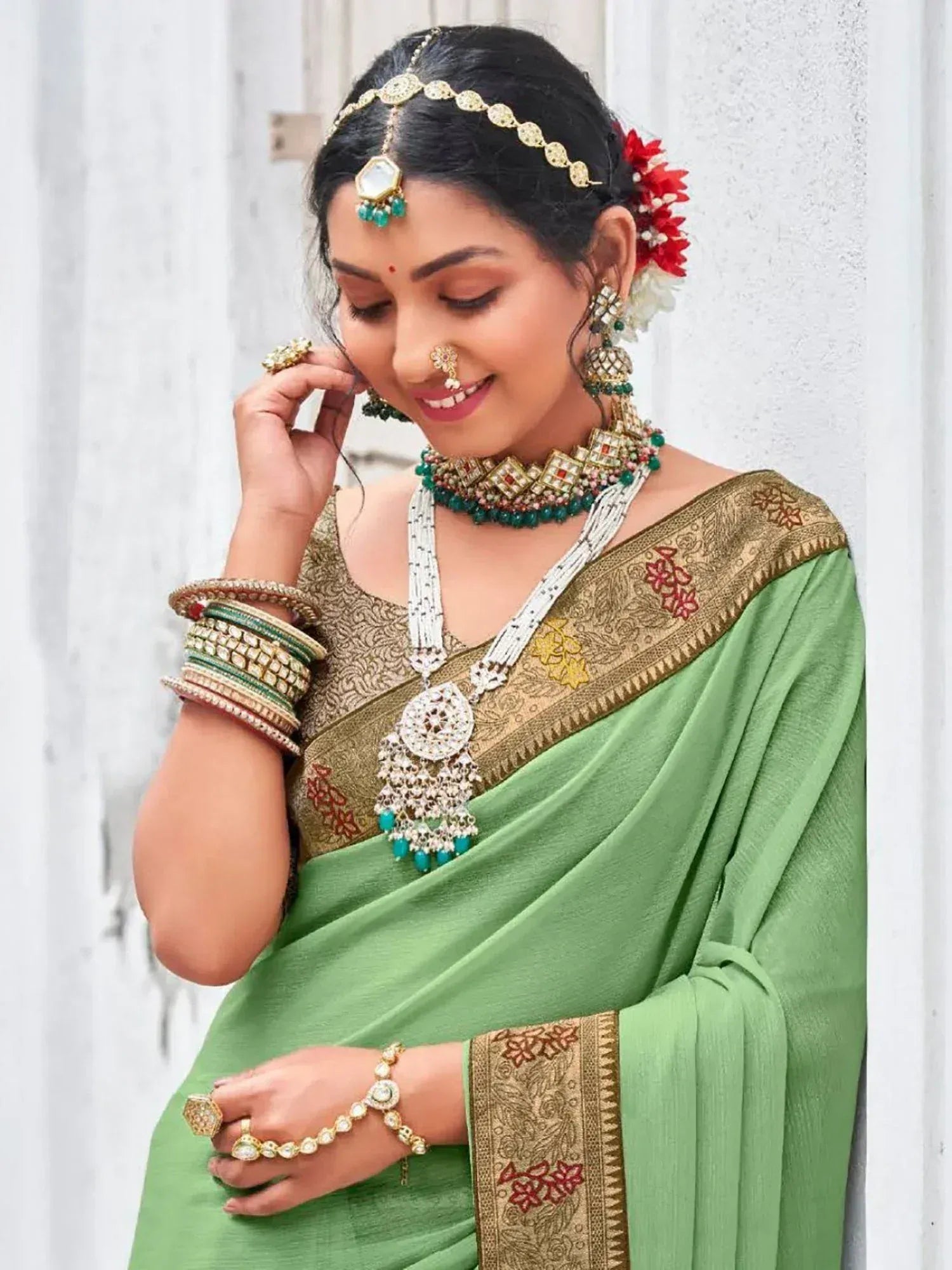 Woman in green ethnic saree with gold embroidery, traditional Indian jewelry, and floral hair accessory