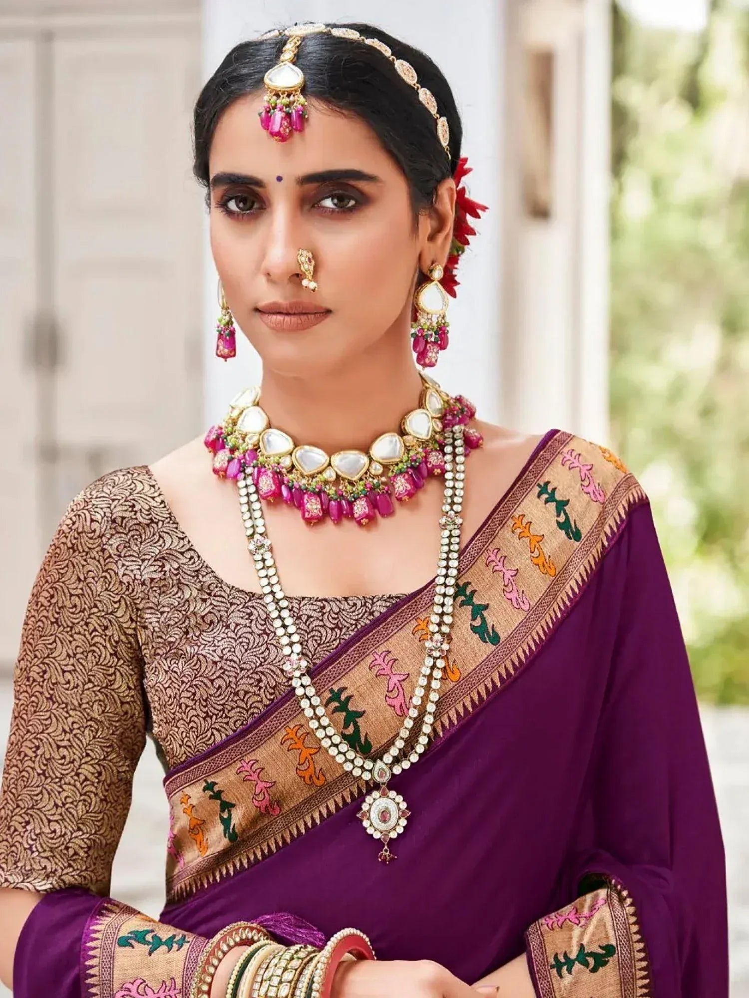Woman in purple embroidered saree with gold blouse, traditional Indian jewelry, and floral hair accessory