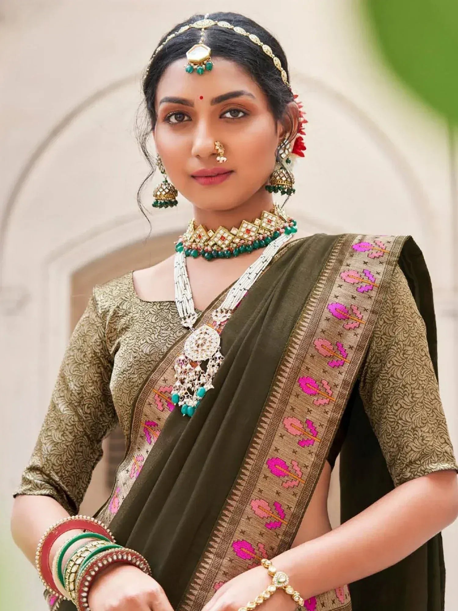 Woman in olive green embroidered saree with gold blouse, traditional Indian jewelry, and floral border