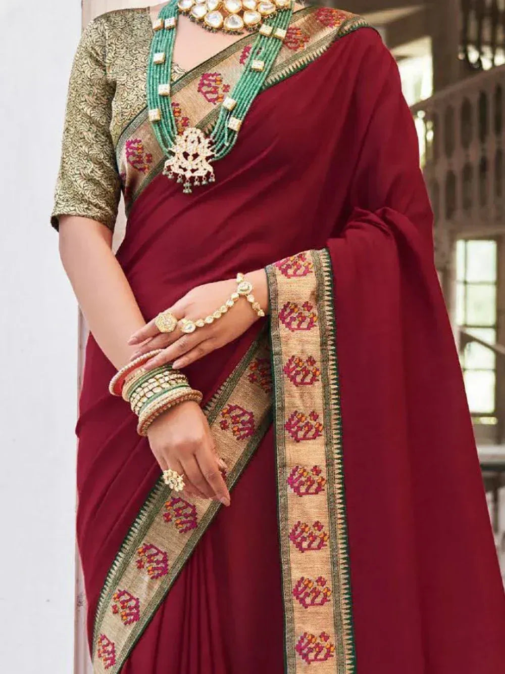 Maroon ethnic saree with gold embroidery, green border, and traditional jewelry for Indian occasions