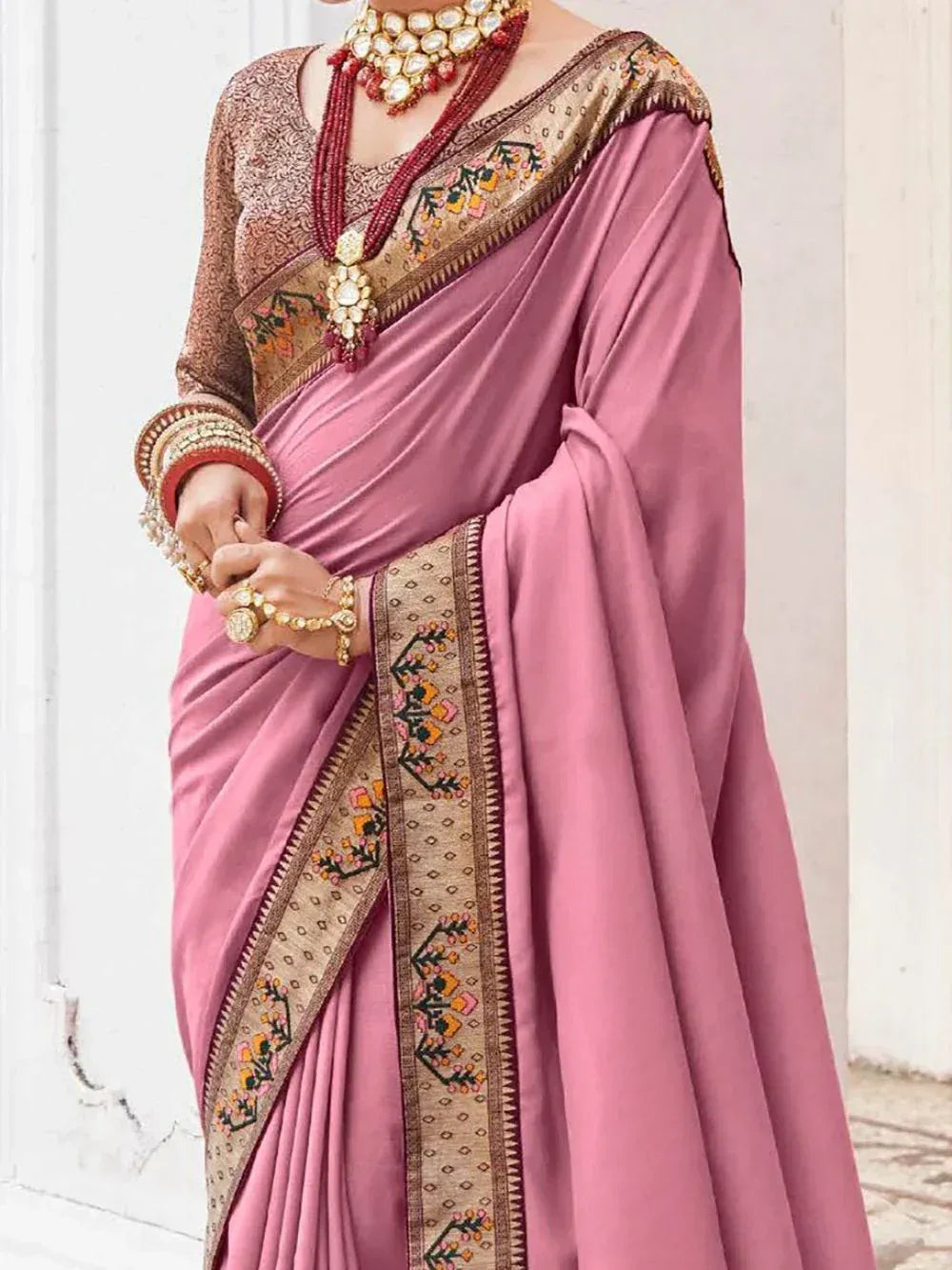 Pink designer saree with embroidered border, paired with traditional jewelry for Indian ethnic wear