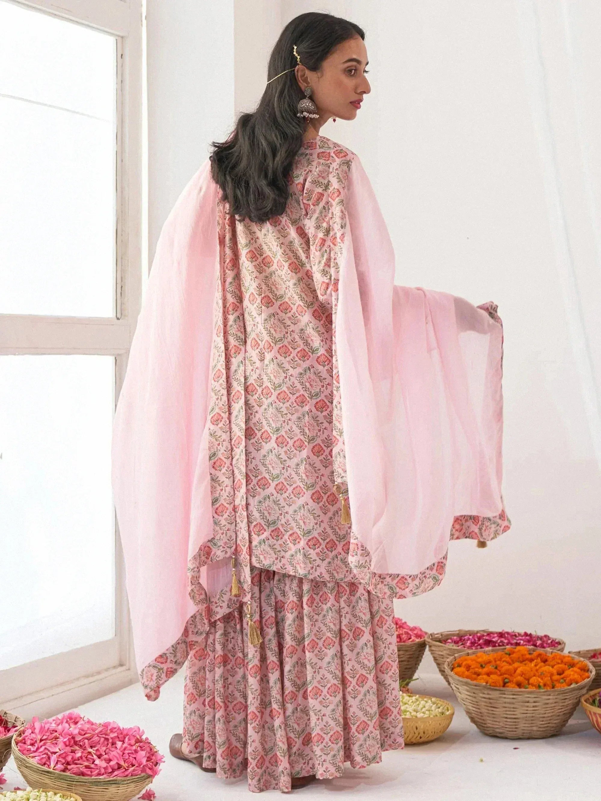 Pink floral printed salwar kameez with matching dupatta, styled with traditional earrings and flower baskets