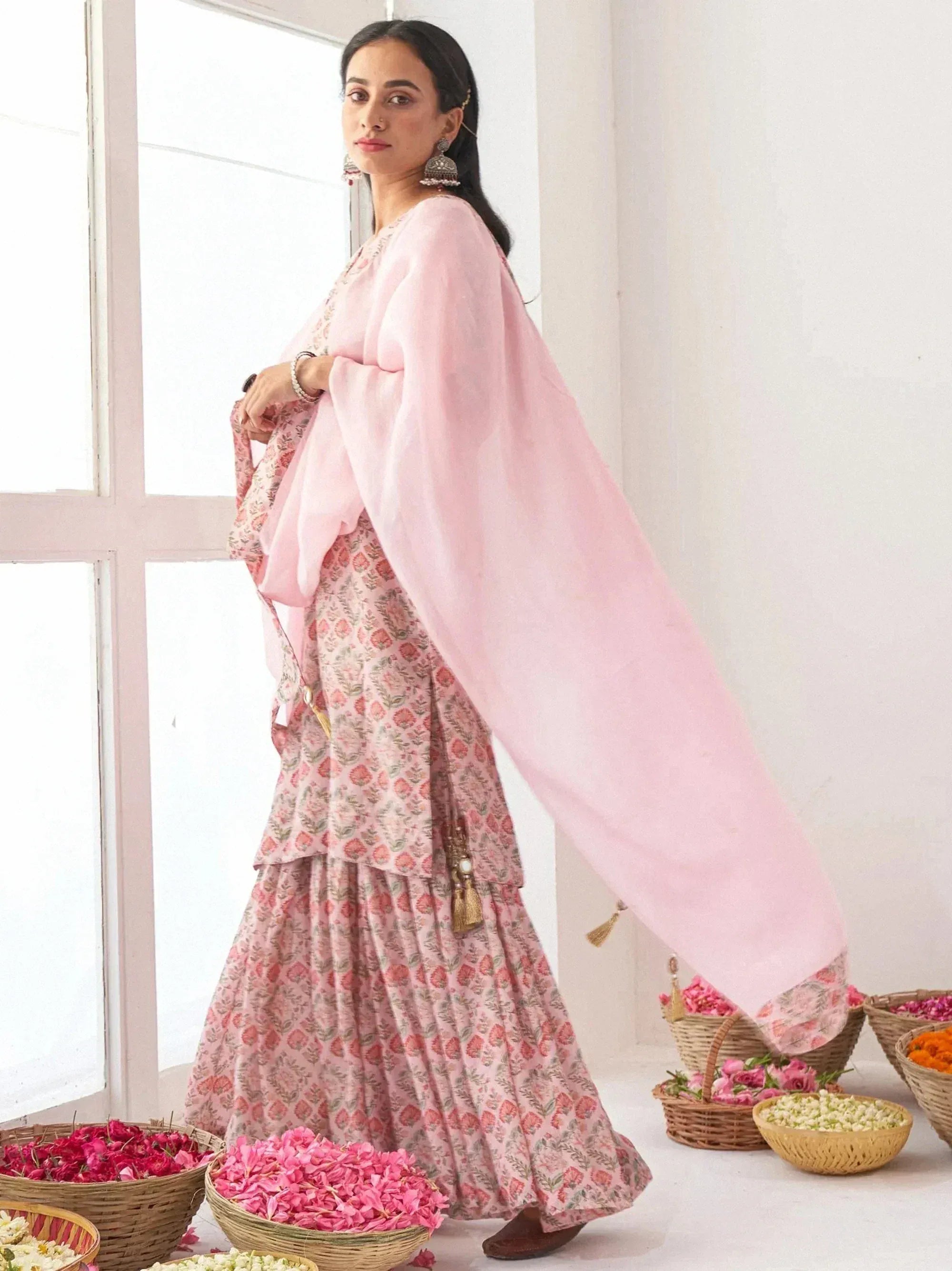 Woman in pink floral ethnic salwar kameez with sheer dupatta, standing near flower baskets