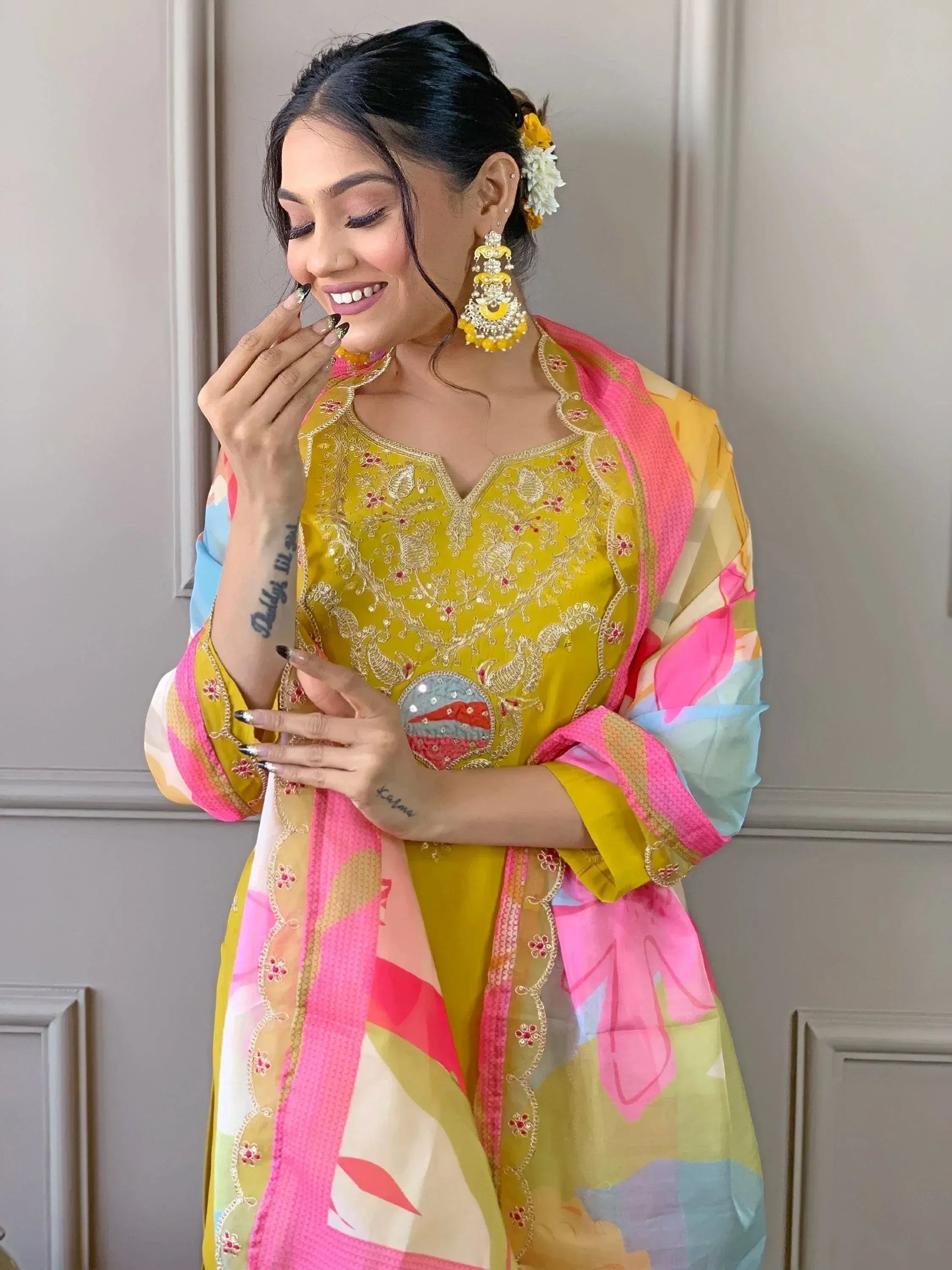 Woman in vibrant yellow embroidered salwar kameez with pink floral dupatta, perfect for festive Indian ethnic wear.