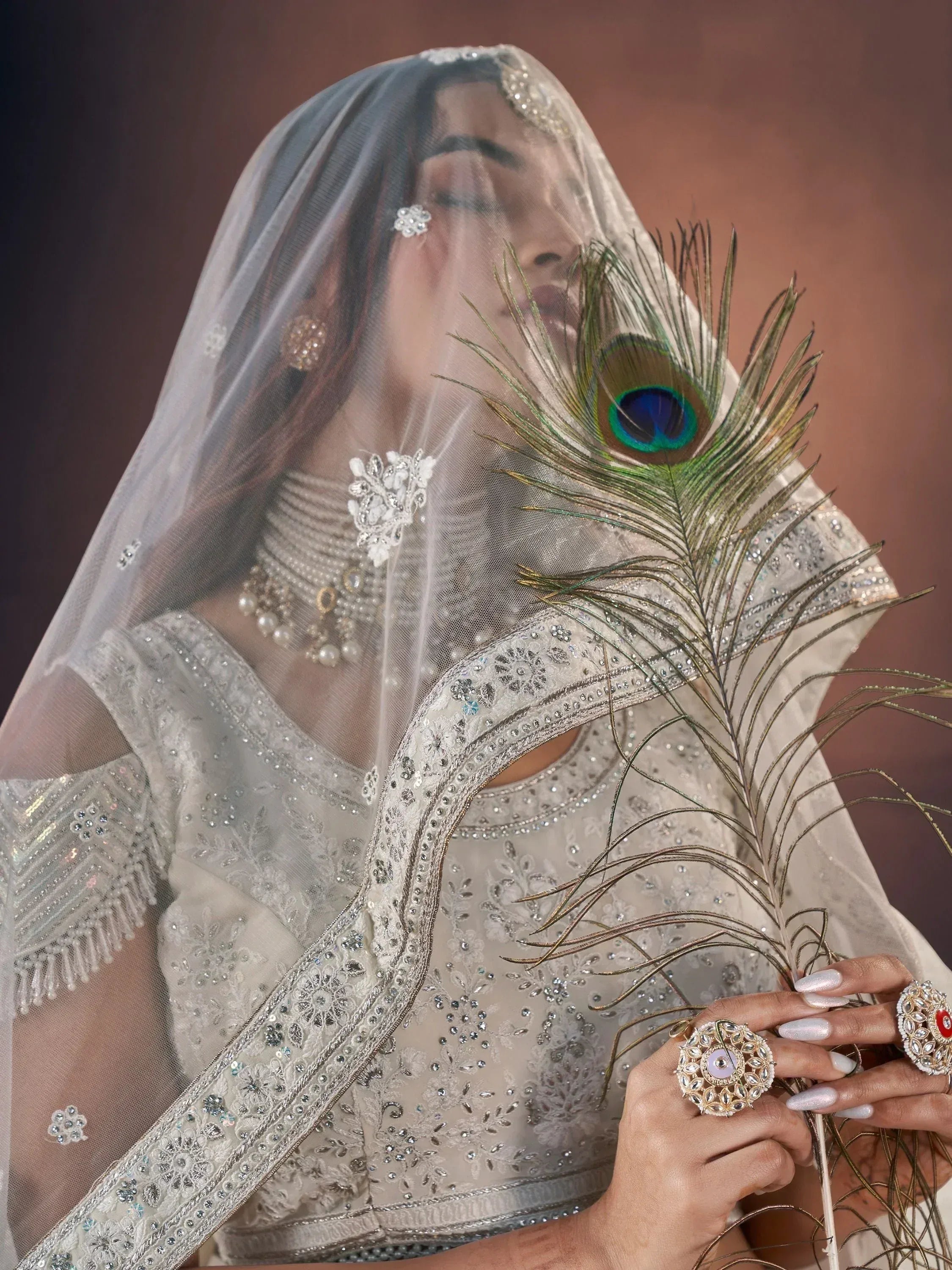 Elegant Indian bridal lehenga with sheer veil, peacock feather, and intricate silver embroidery for wedding wear