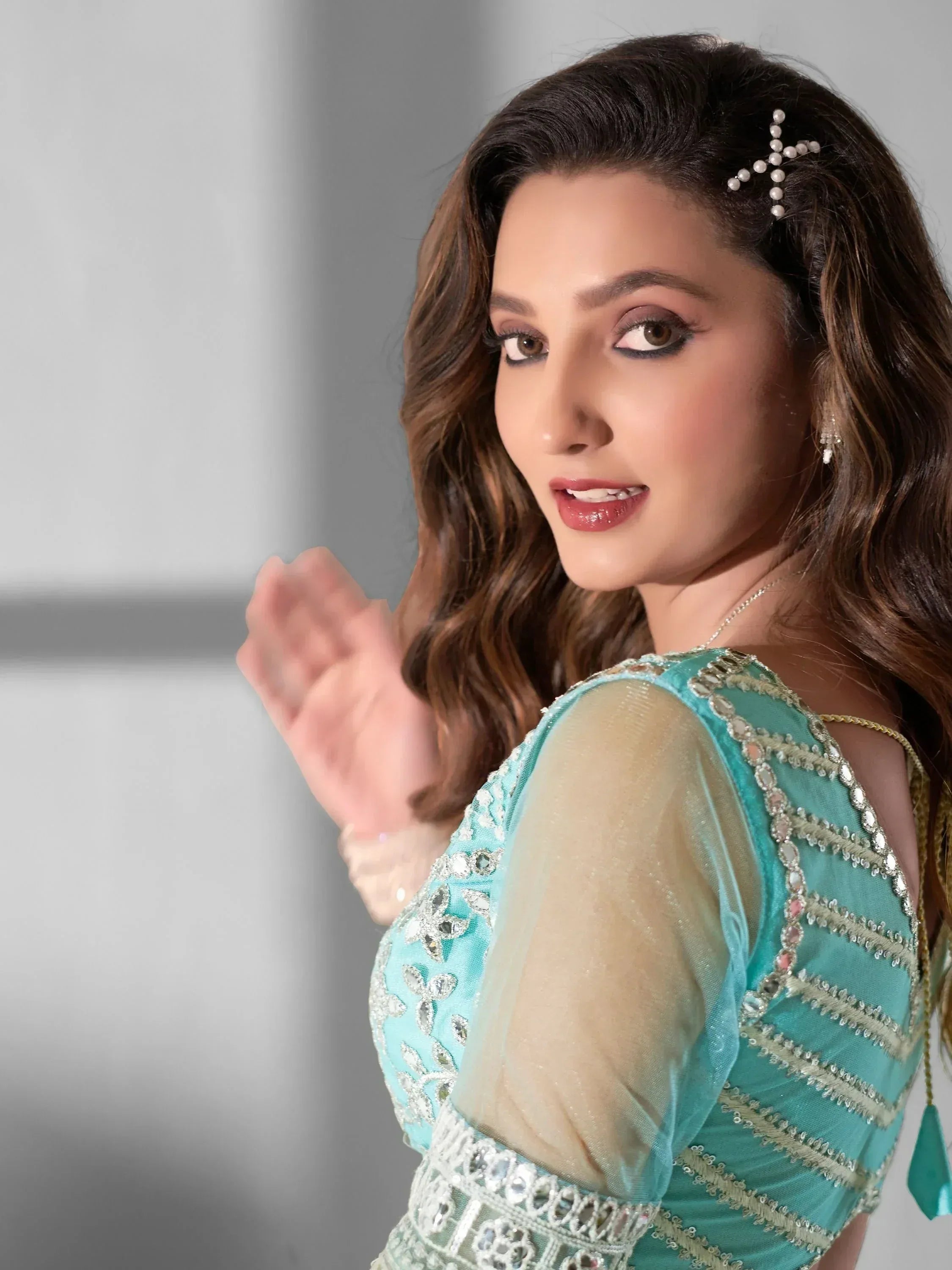 Woman in turquoise embroidered ethnic gown with sheer sleeves and pearl hair accessory