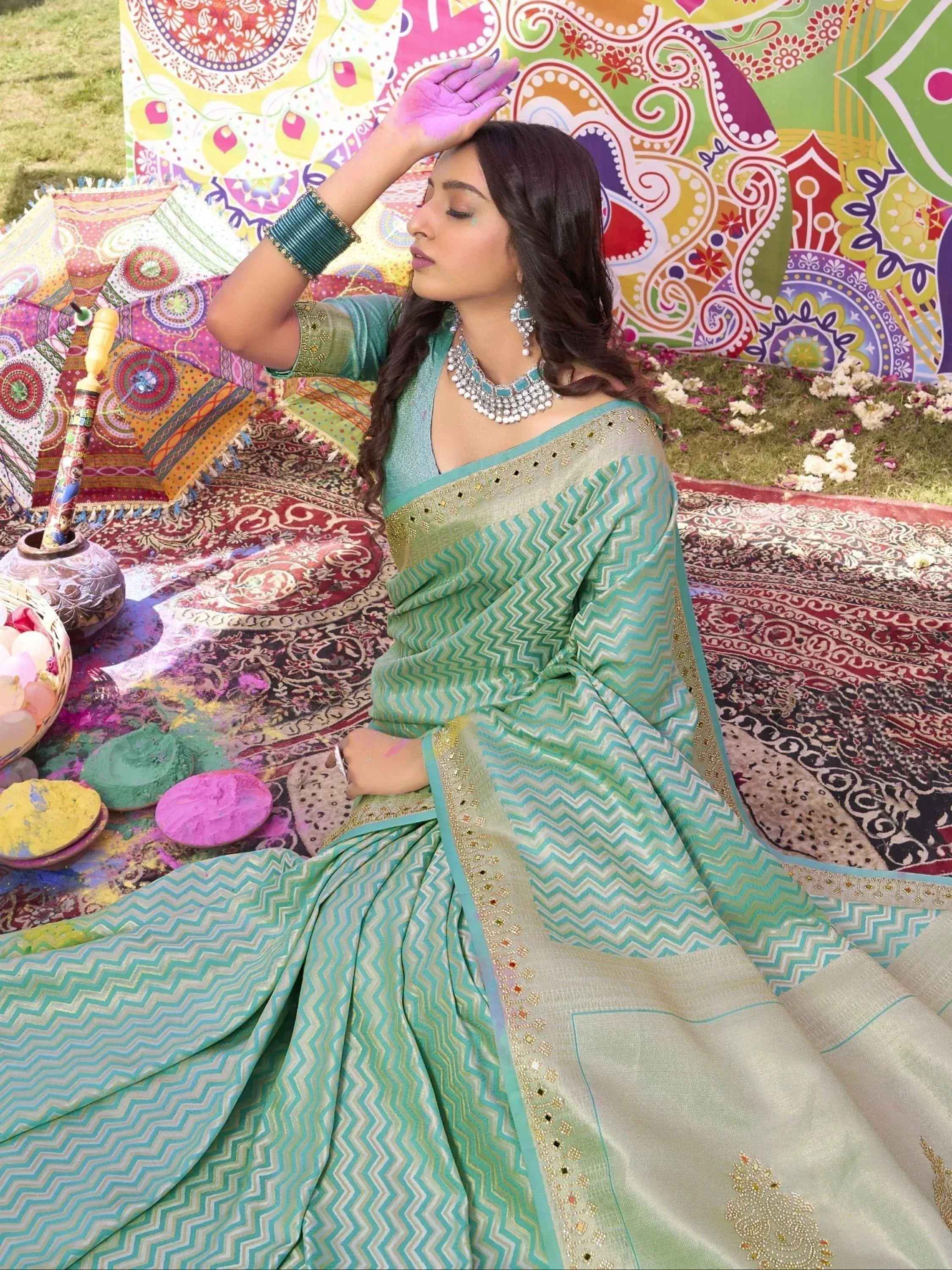 Woman in turquoise zigzag saree with Holi colors, ethnic jewelry, and festive backdrop