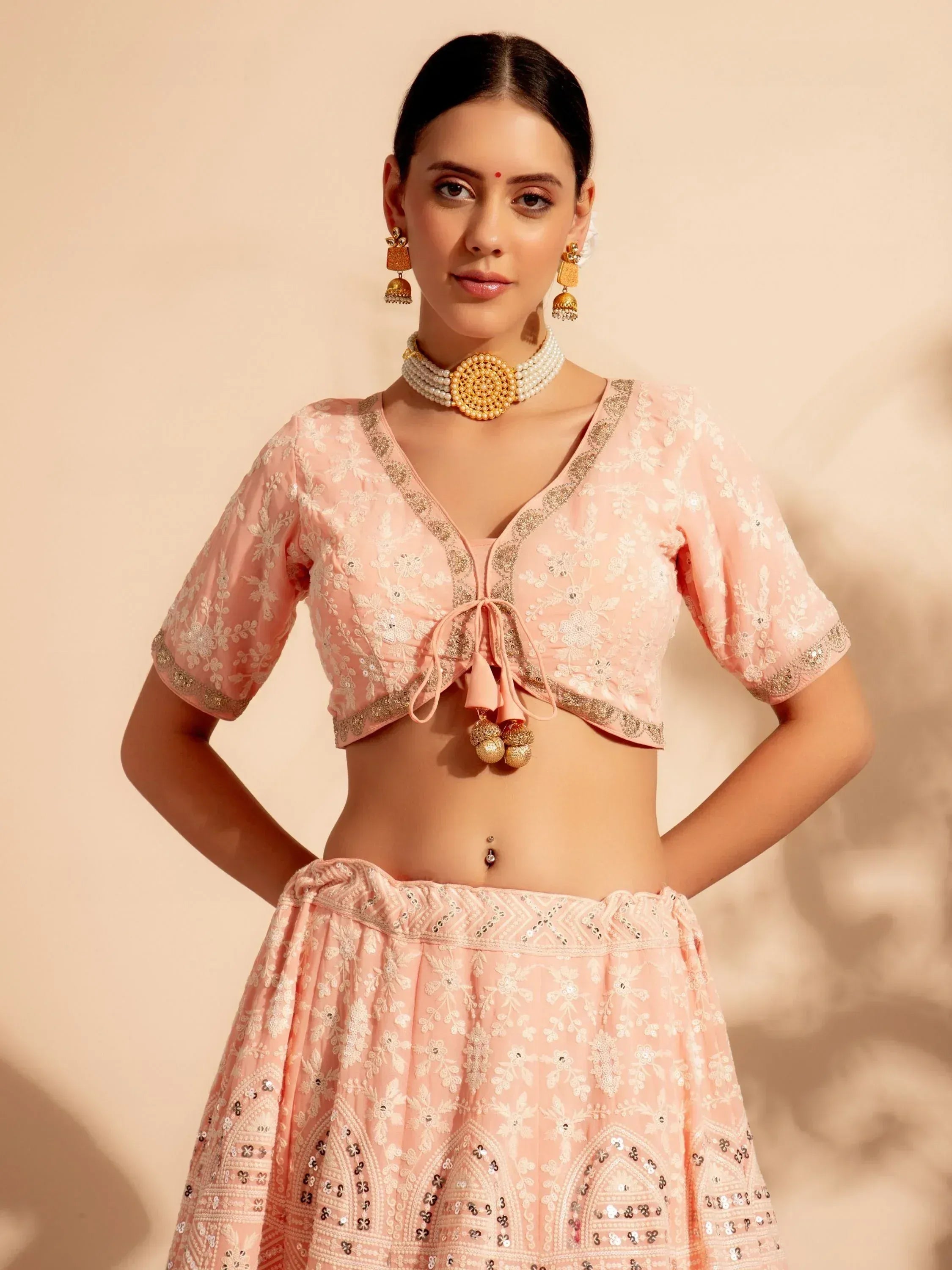 Pink embroidered lehenga choli with floral motifs and gold detailing, paired with traditional jewelry