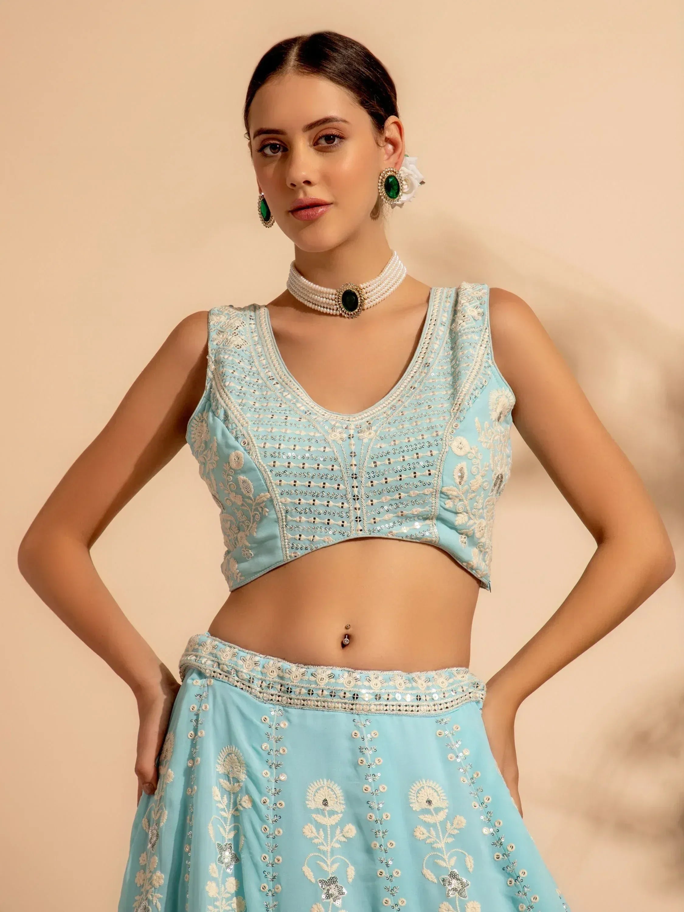 Light blue embroidered lehenga choli with floral motifs and mirror work, paired with pearl choker and green earrings.
