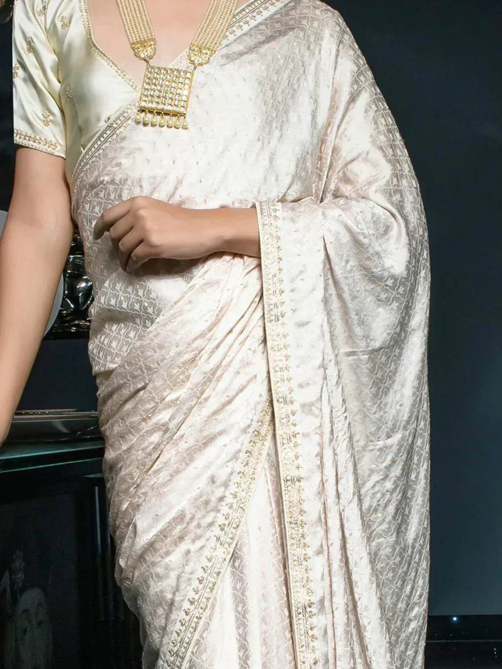 Elegant cream silk saree with gold embroidery, paired with matching blouse and statement necklace