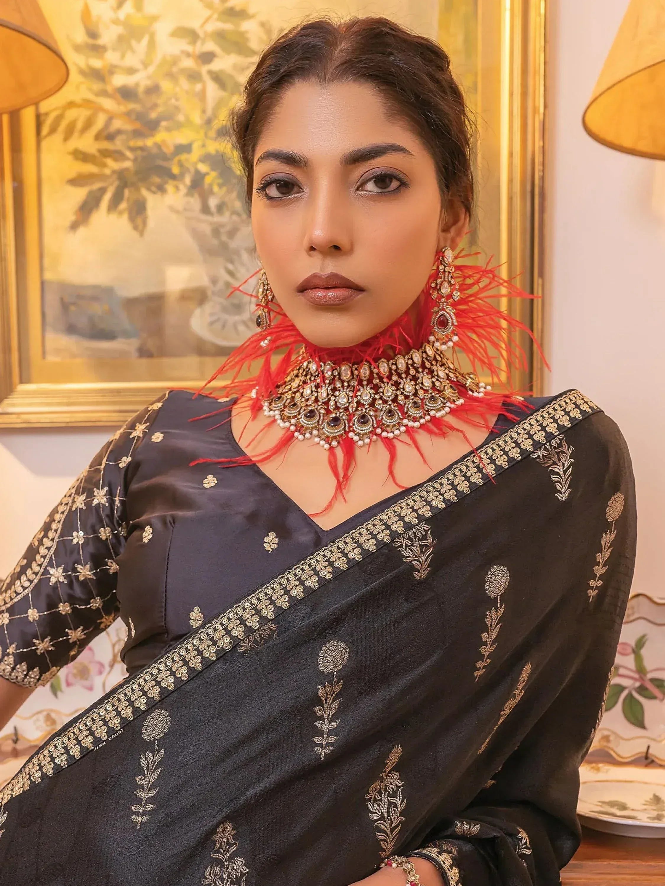 Woman in black embroidered saree with gold detailing and red feather jewelry, elegant Indian ethnic wear.