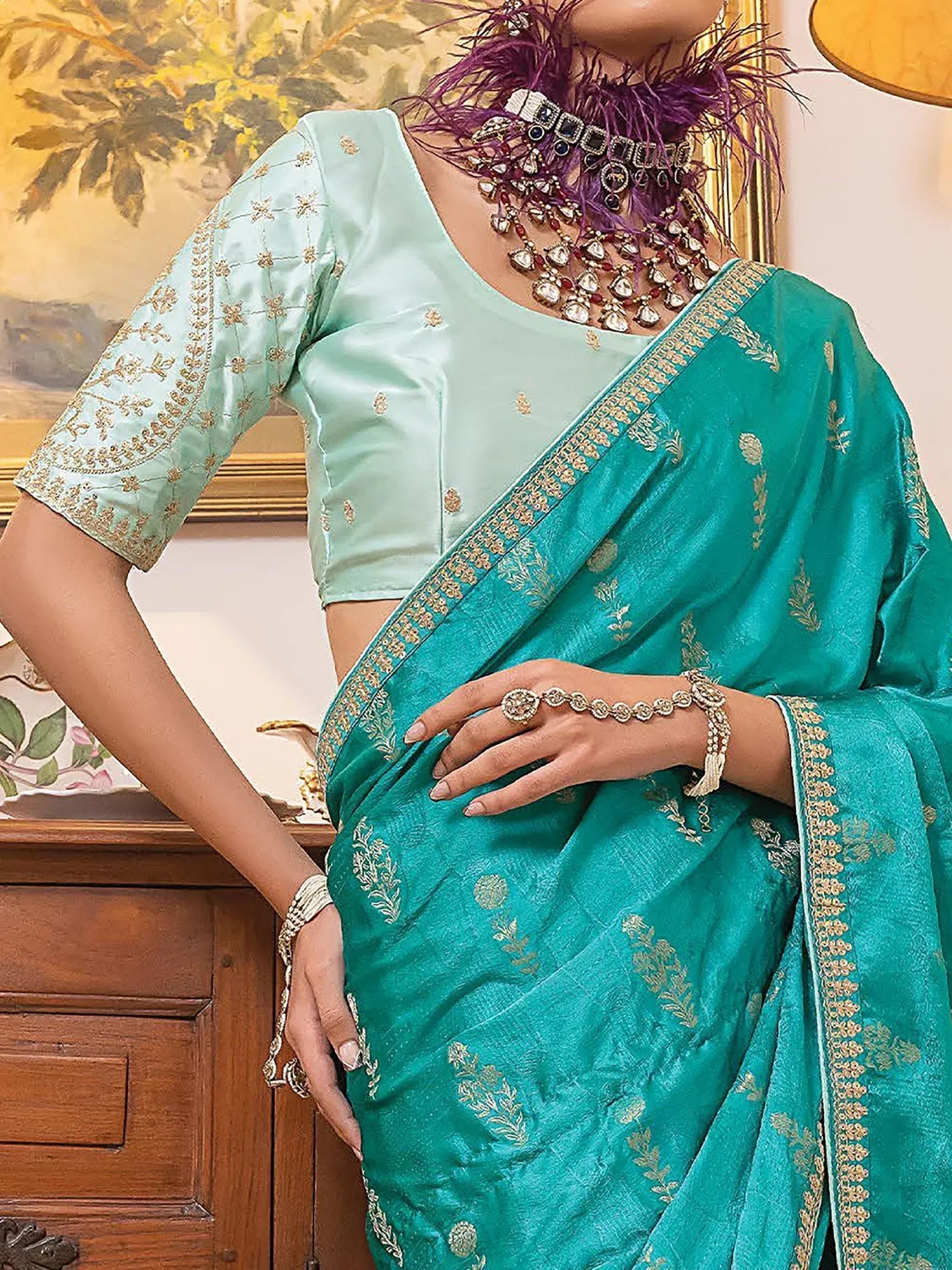 Teal embroidered saree with gold detailing, paired with light blue blouse and statement jewelry for ethnic wear.