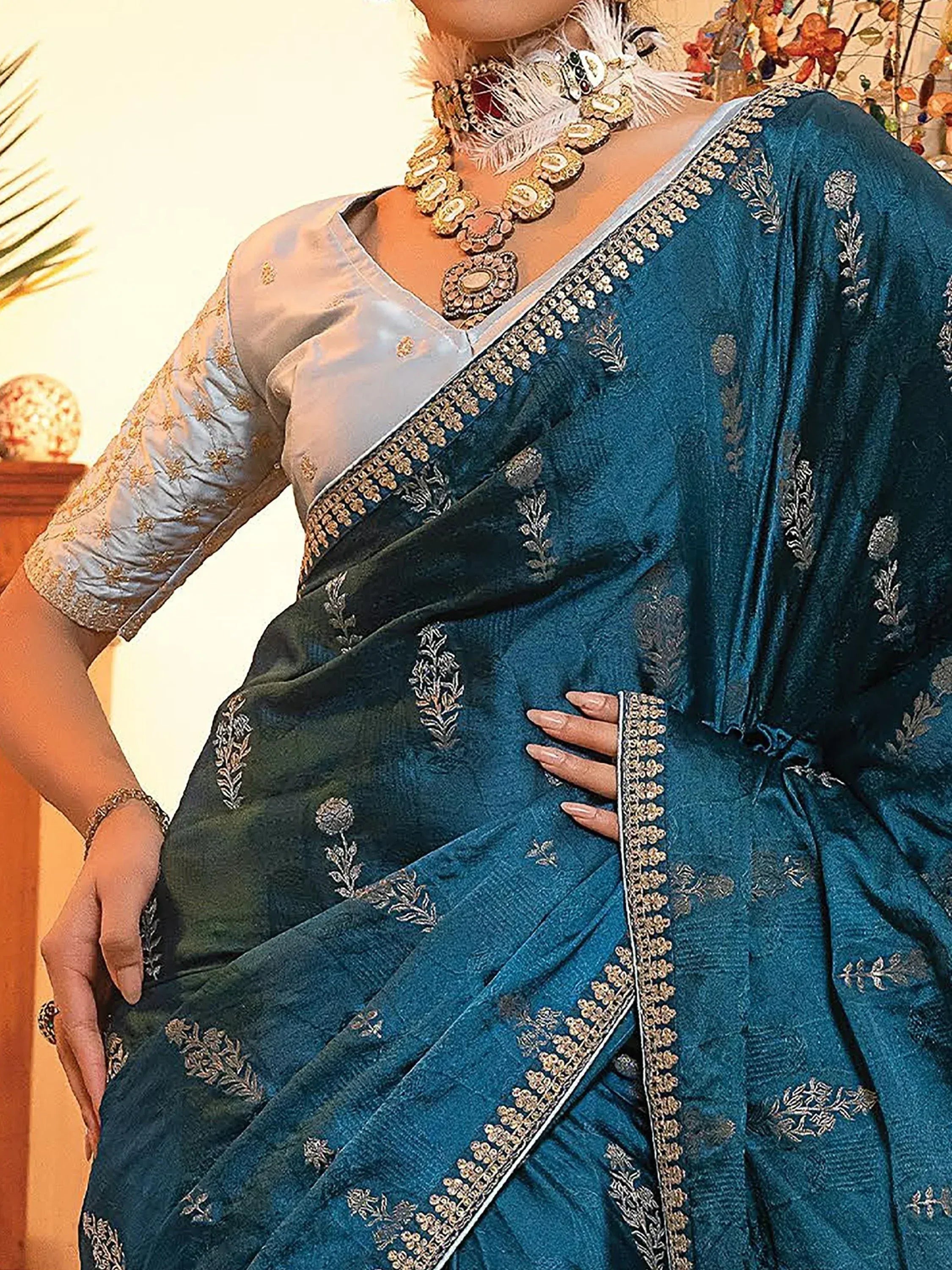 Teal embroidered saree with gold detailing, paired with a light blue blouse and statement jewelry.