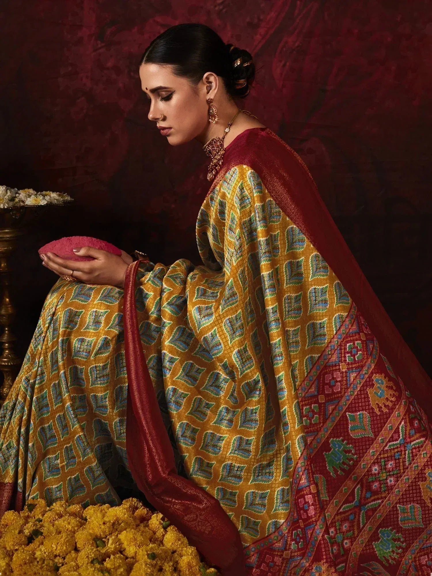 Woman in designer ethnic saree with gold and red pattern, traditional jewelry, marigold flowers
