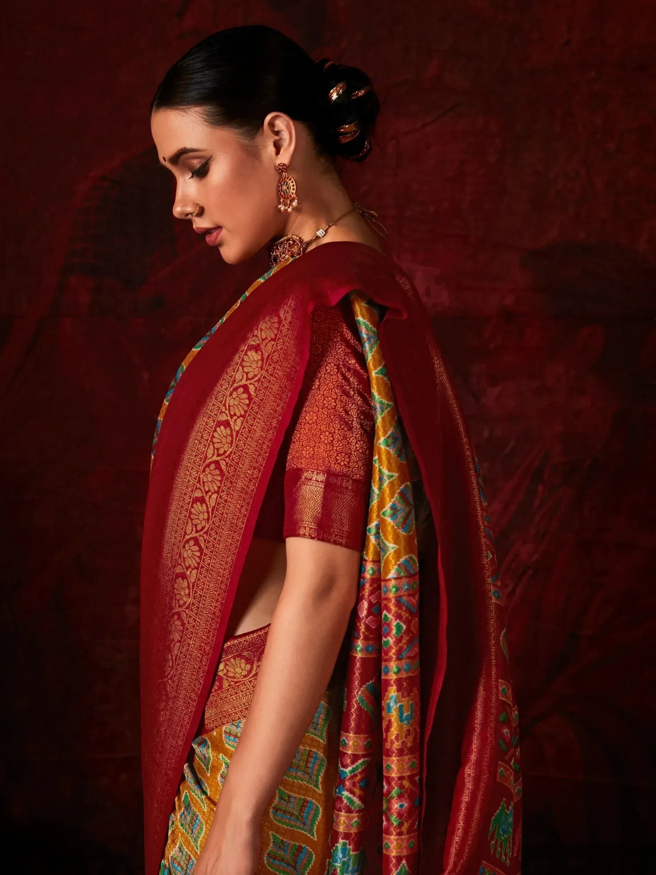 Woman in red and gold designer saree with intricate patterns, traditional jewelry, and elegant bun hairstyle