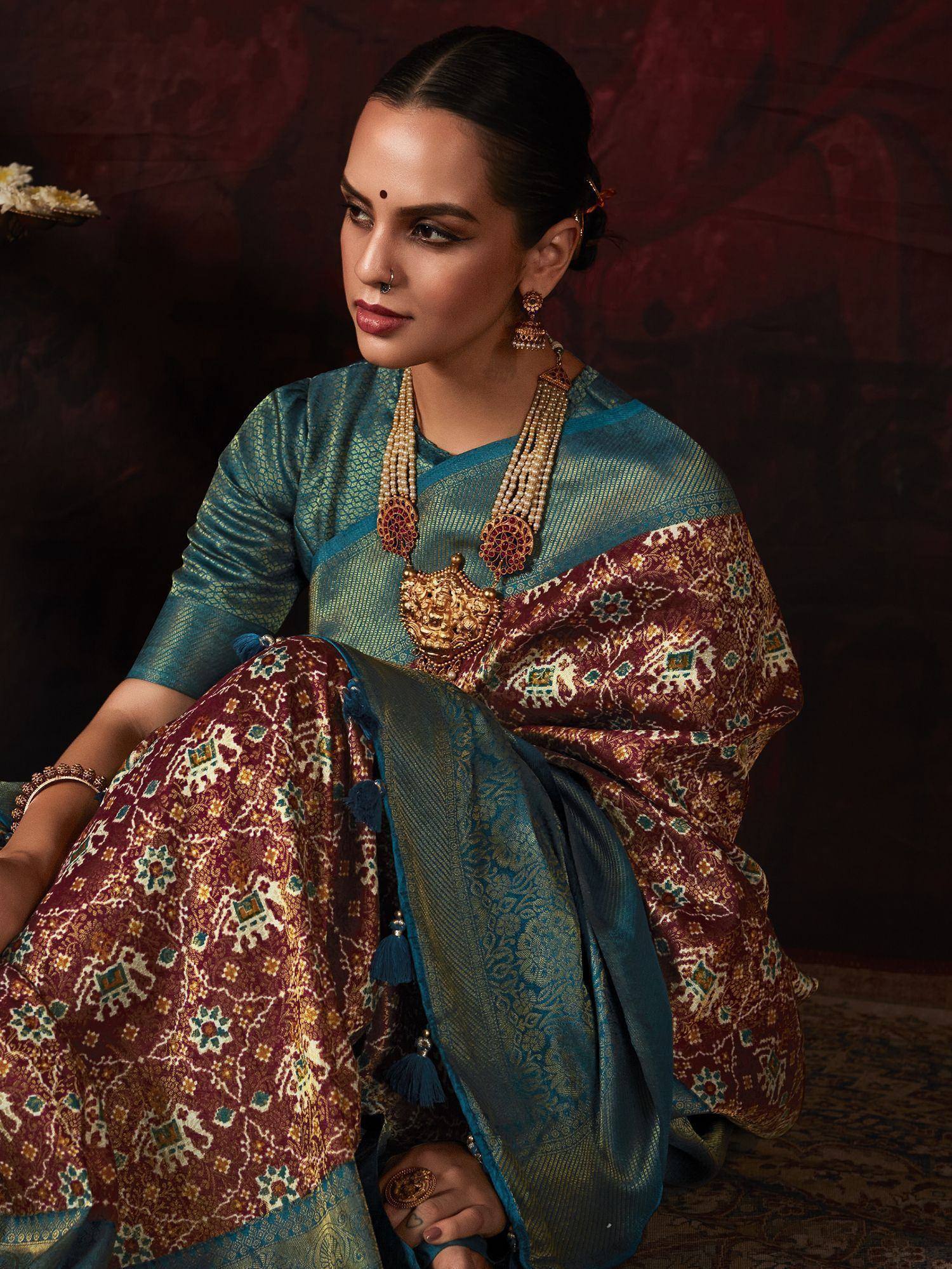 Woman in teal and maroon designer saree with gold jewelry, ethnic Indian wear