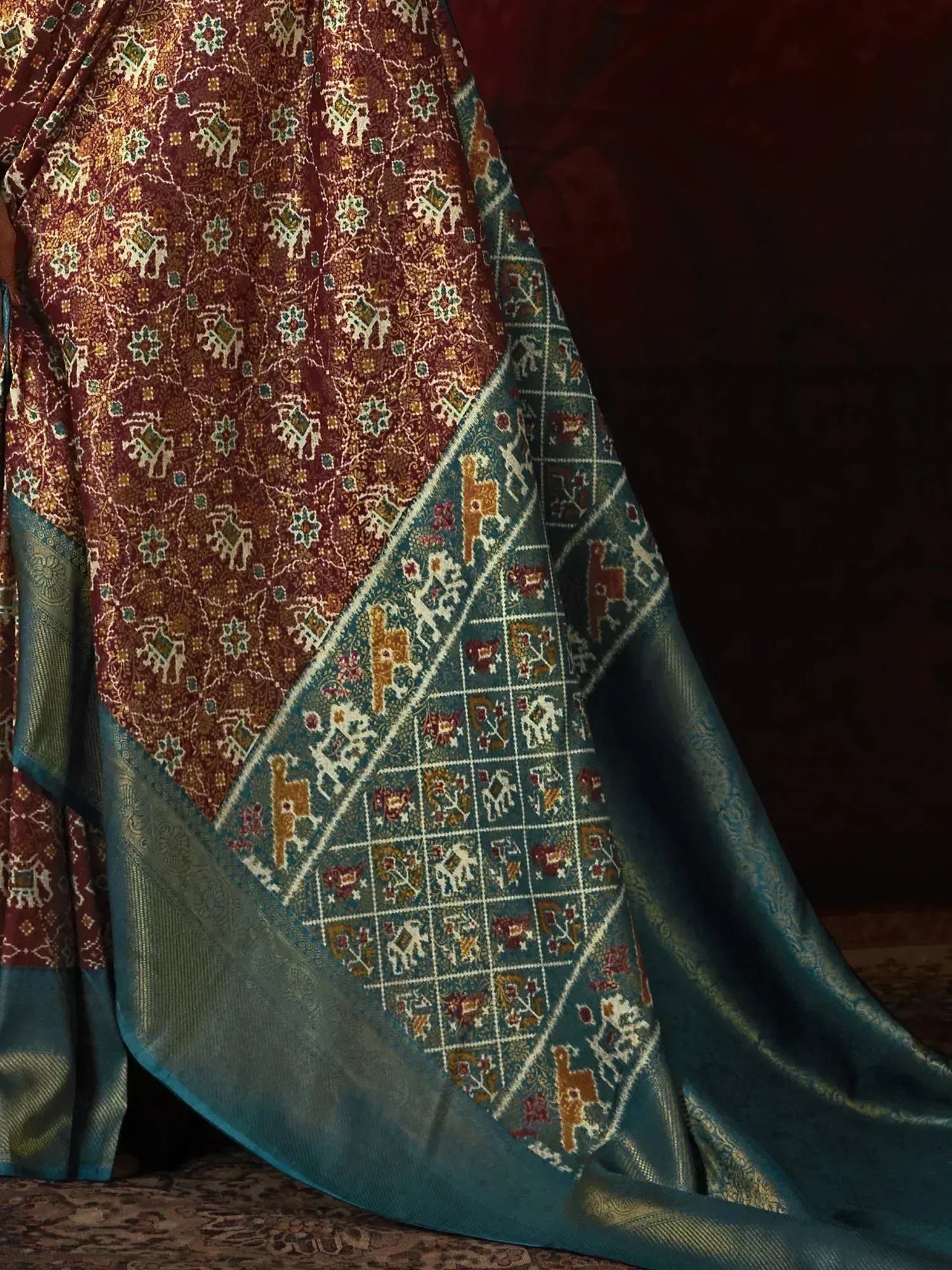 Rich maroon and teal ethnic saree with intricate elephant and floral motifs, perfect for Indian celebrations.