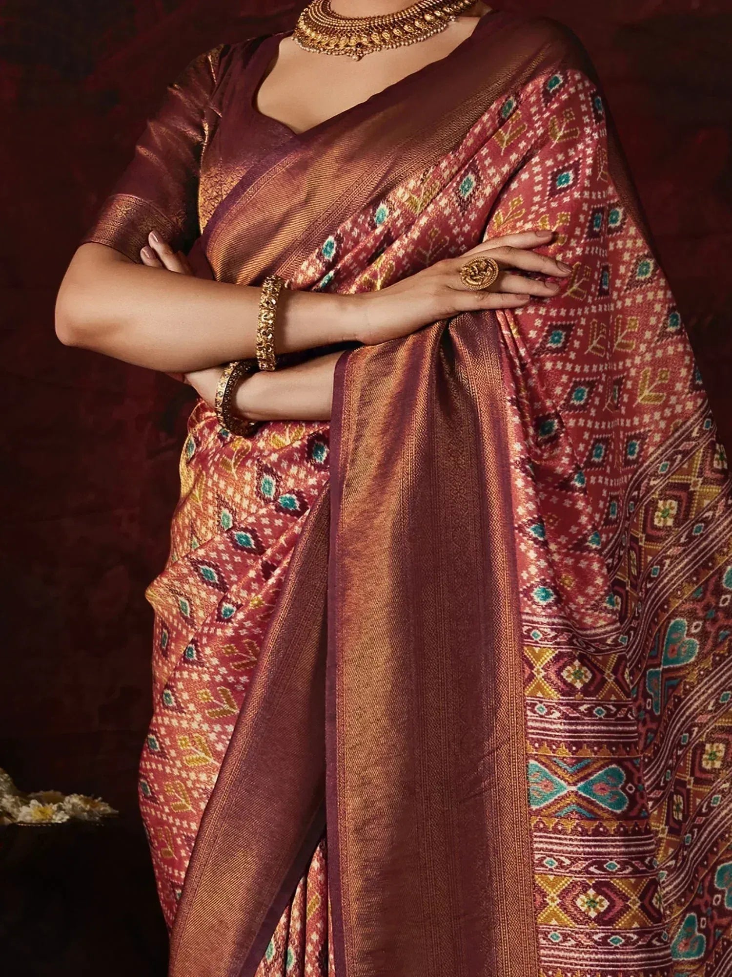 Rich maroon ethnic saree with intricate geometric patterns and gold border, paired with traditional jewelry
