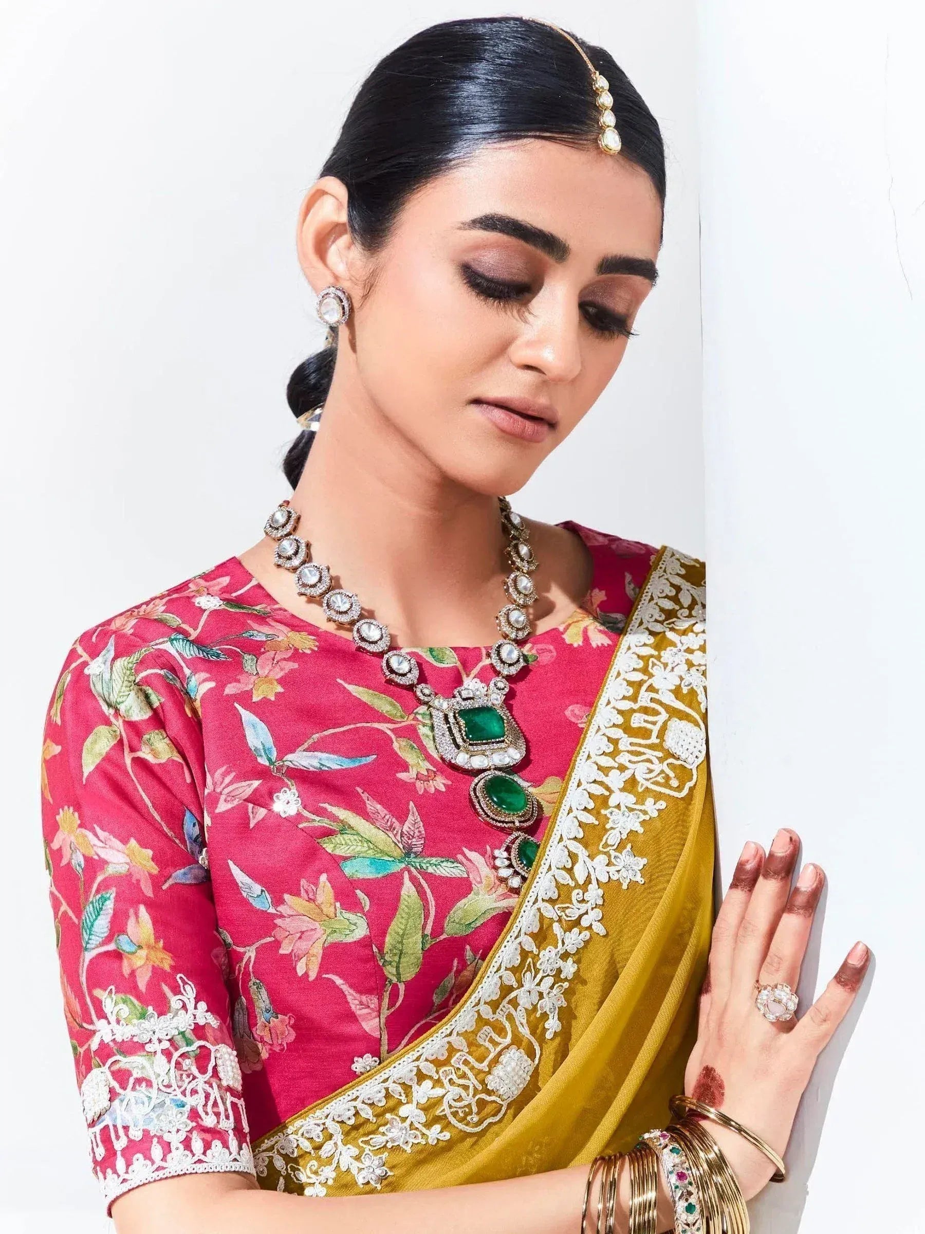 Woman in floral pink blouse and gold saree with emerald jewelry, traditional Indian ethnic wear
