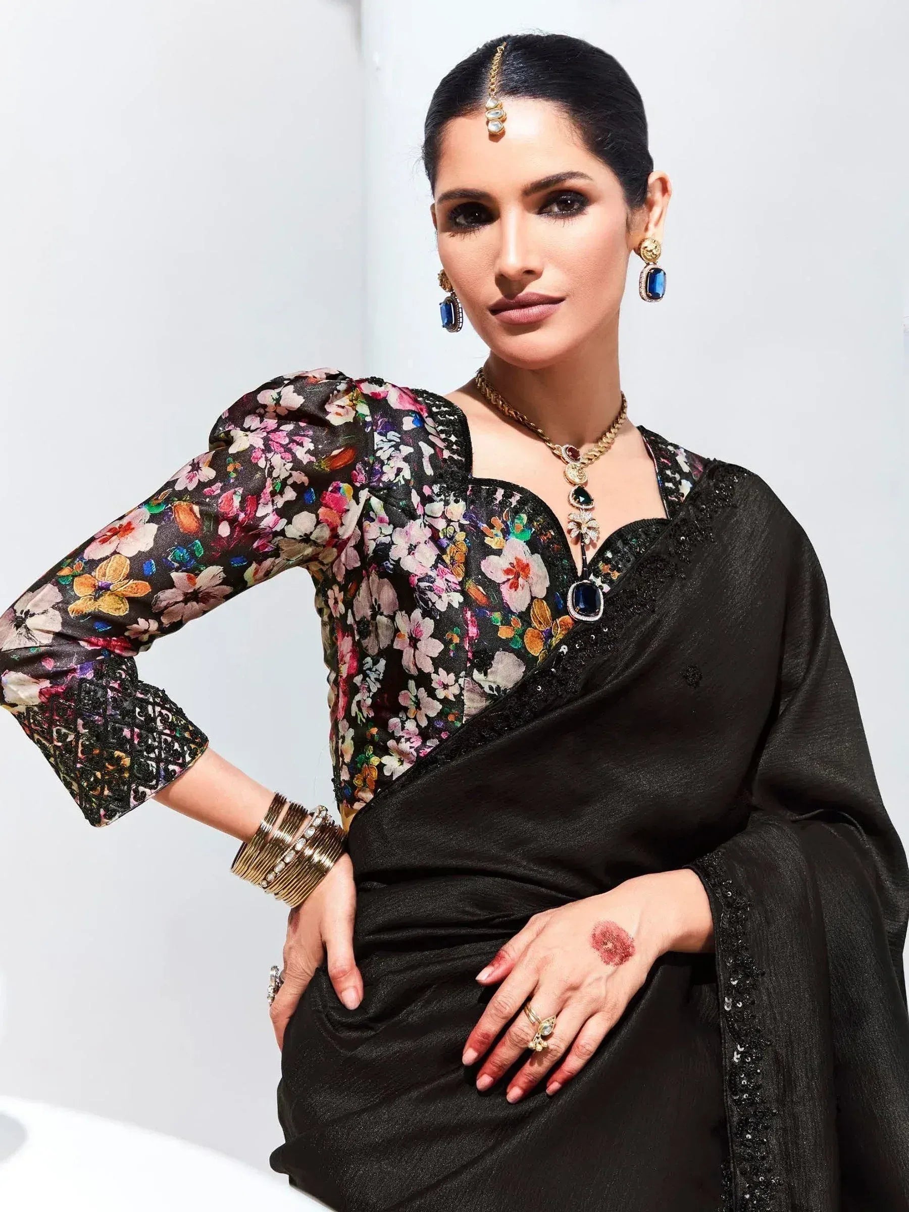 Elegant woman in black saree with floral blouse, statement jewelry, and traditional Indian accessories.
